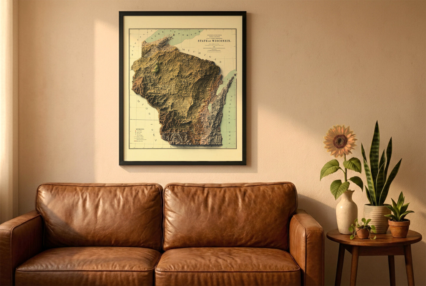 Wisconsin vintage relief map in a black frame above a brown leather sofa. Boho living room with warm sunlight, sunflower, and indoor plants on a wooden side table