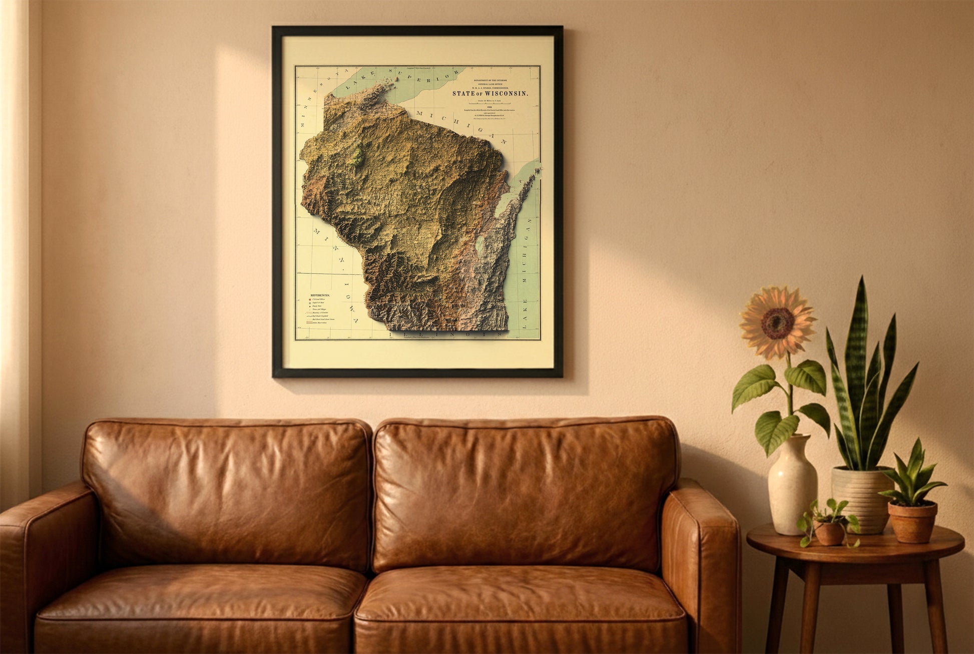 Wisconsin vintage relief map in a black frame above a brown leather sofa. Boho living room with warm sunlight, sunflower, and indoor plants on a wooden side table