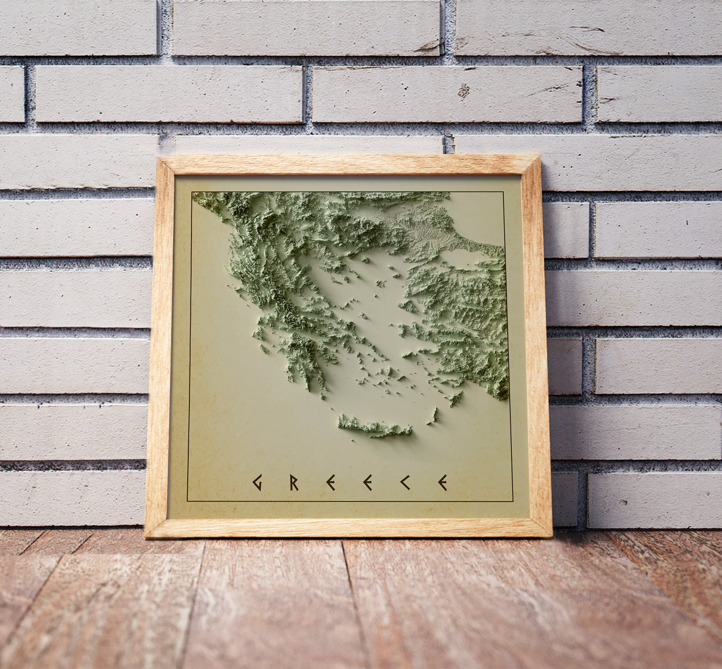 Vintage Greece shaded relief map in a wooden frame. Realistic terrain art print for home decor, displayed against a brick wall