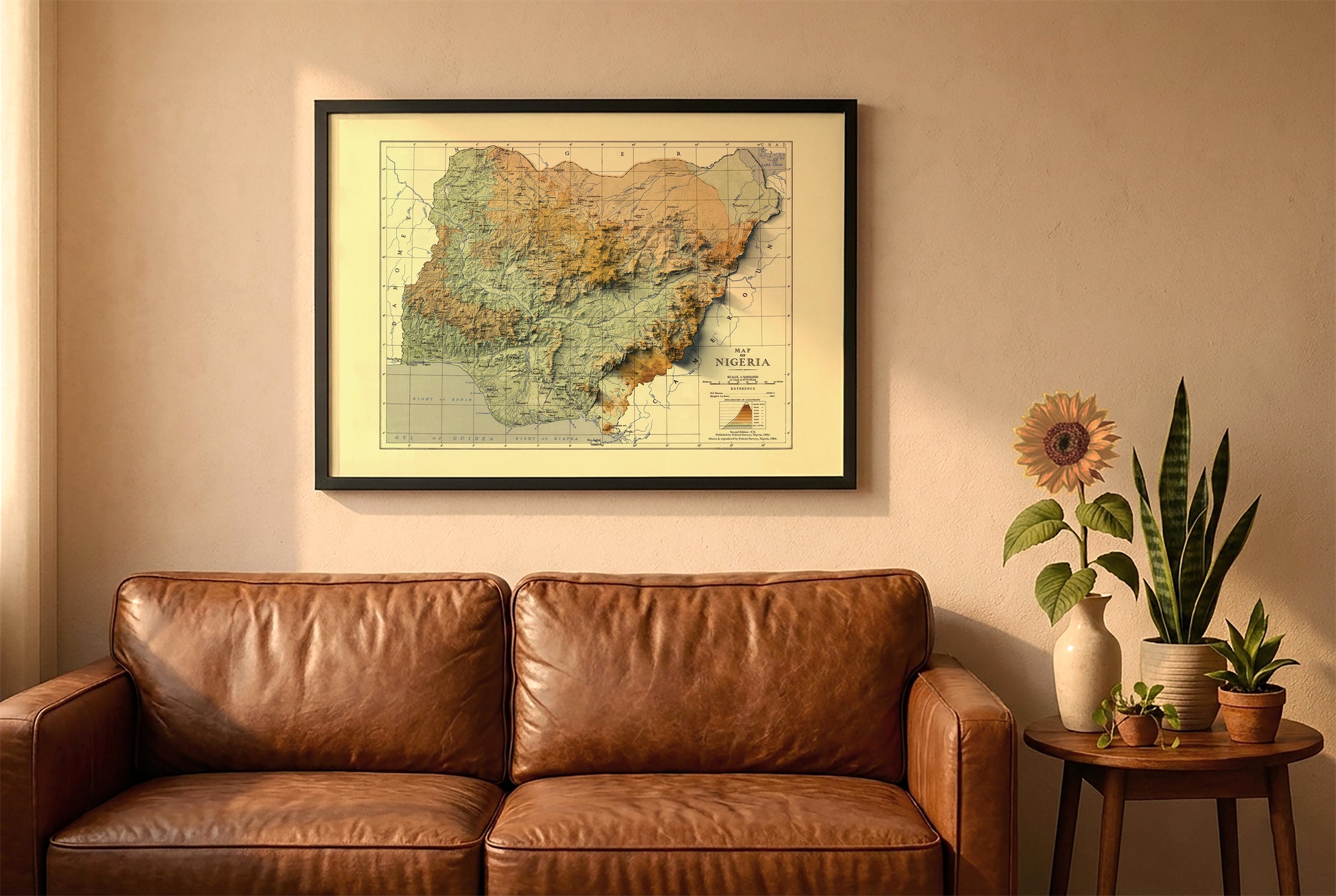 Nigeria vintage relief map in a black frame above a brown leather sofa. Boho living room with warm sunlight, sunflower, and indoor plants on a wooden side table