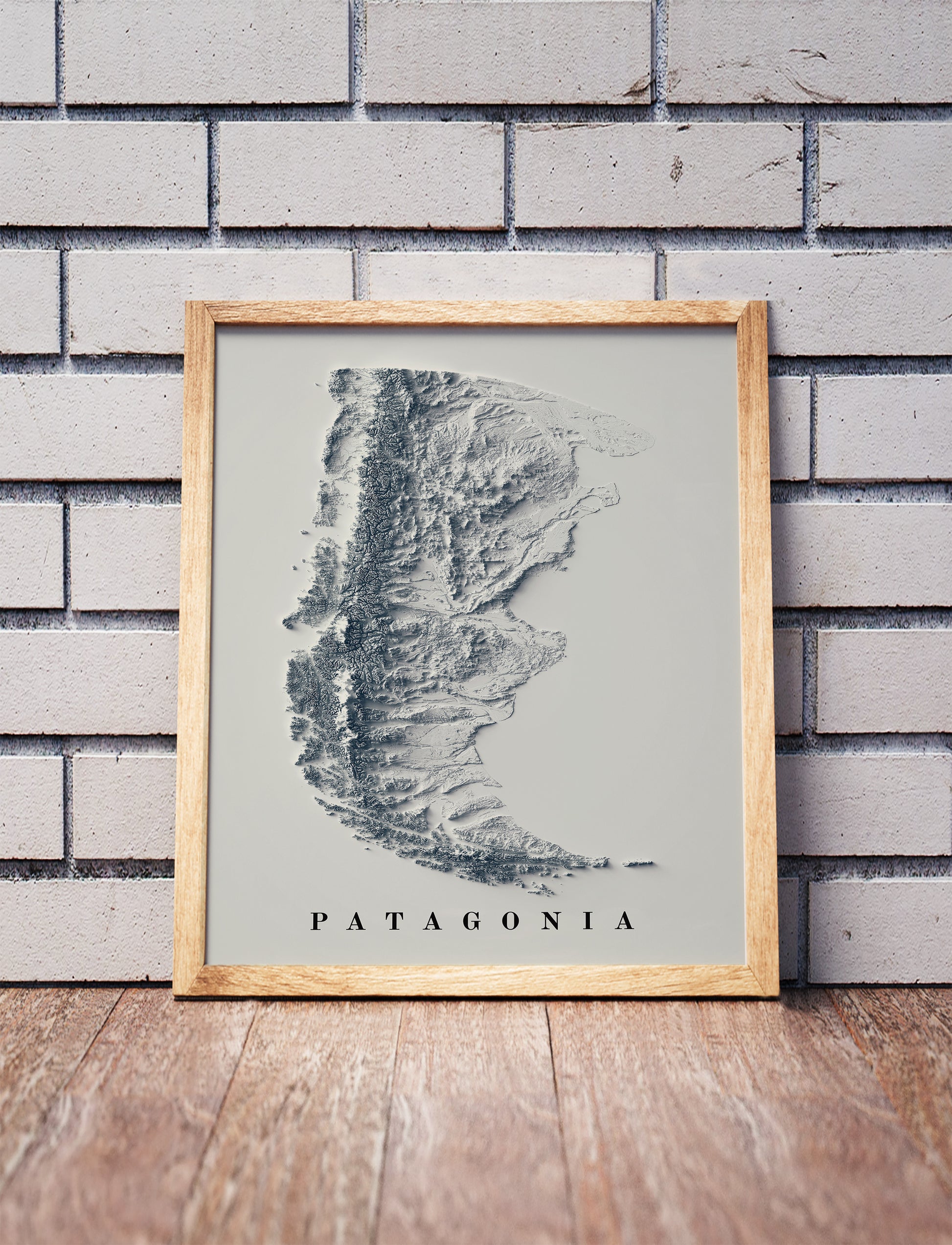 Patagonia shaded relief map in a wooden frame. Realistic terrain art print for home decor, displayed against a brick wall