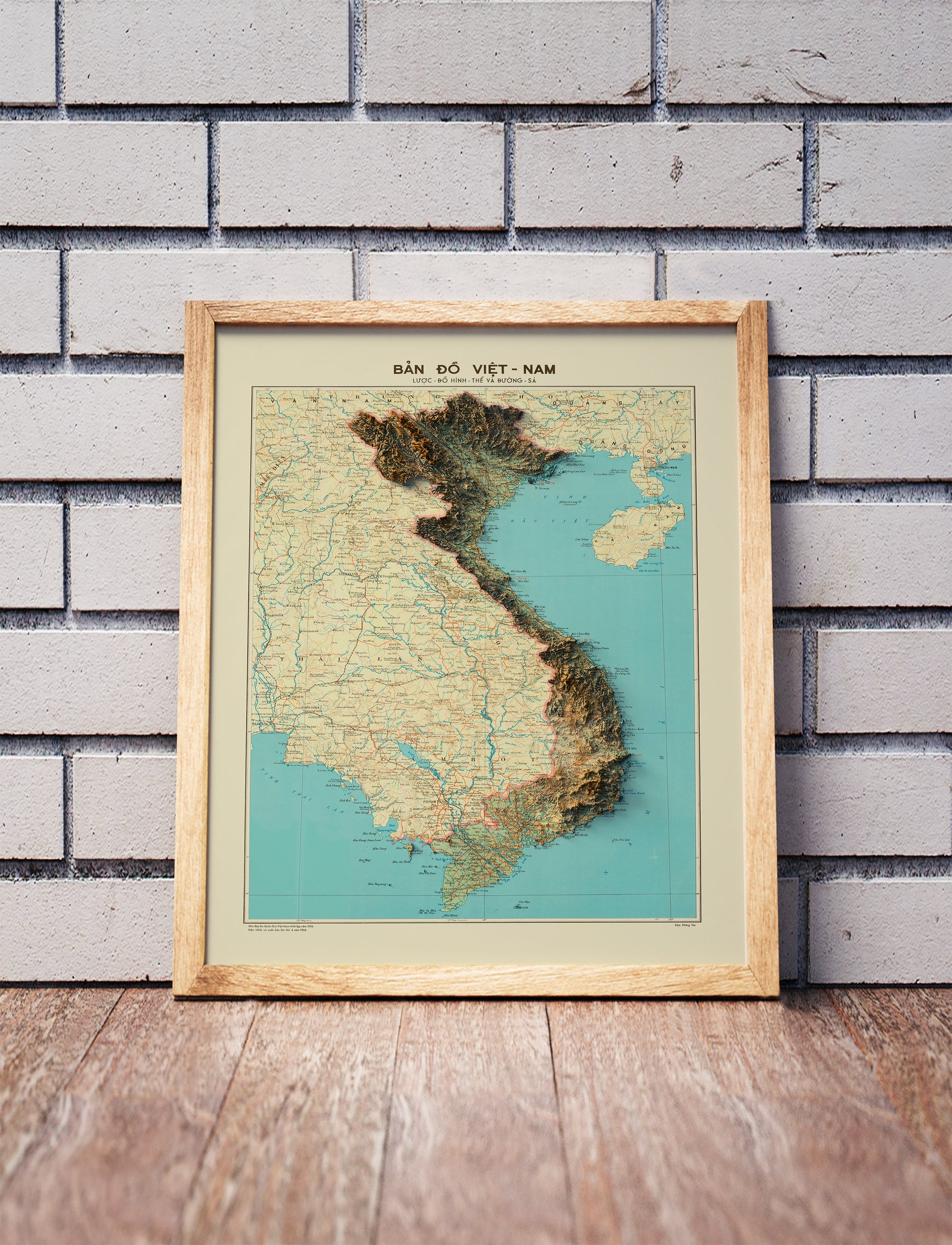 Vintage Vietnam shaded relief map in a wooden frame. Realistic terrain art print for home decor, displayed against a brick wall