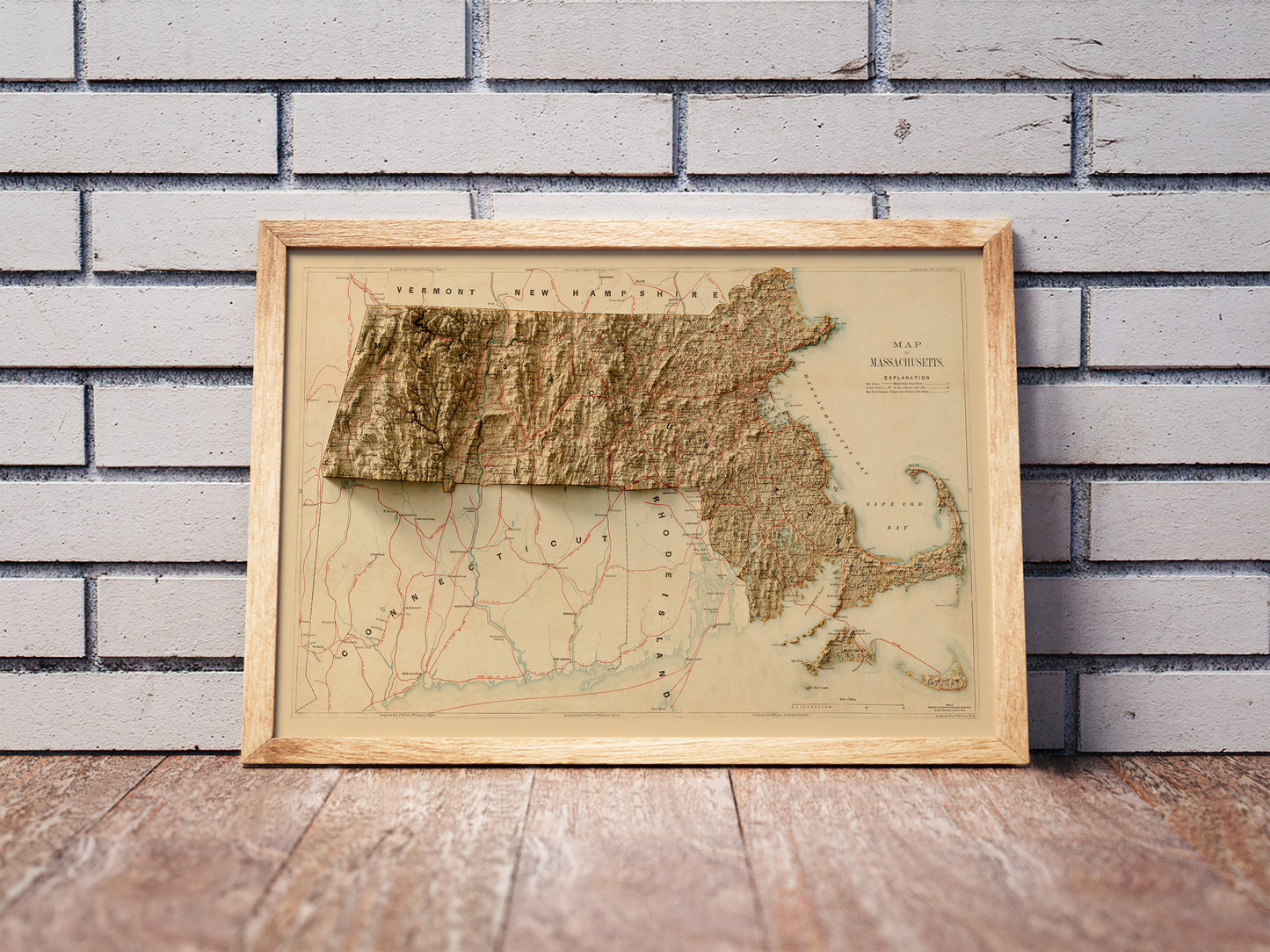 Vintage Massachusetts shaded relief map in a wooden frame. Realistic terrain art print for home decor, displayed against a brick wall