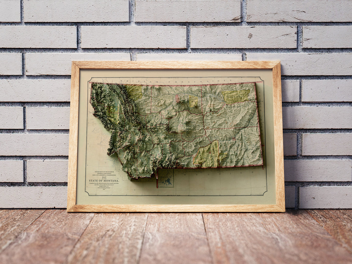 Vintage Montana shaded relief map in a wooden frame. Realistic terrain art print for home decor, displayed against a brick wall