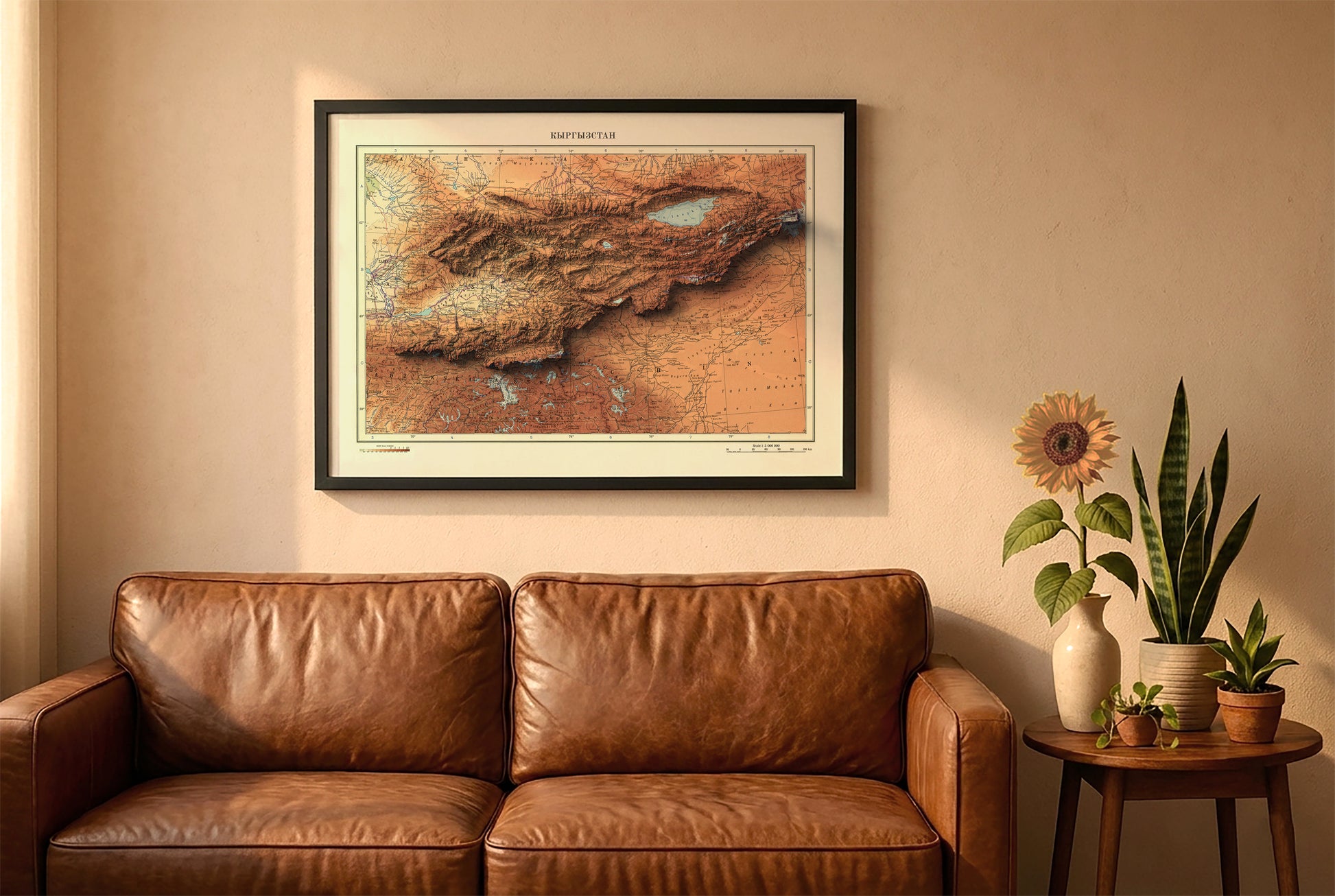 Kyrgyzstan vintage relief map in a black frame above a brown leather sofa. Boho living room with warm sunlight, sunflower, and indoor plants on a wooden side table