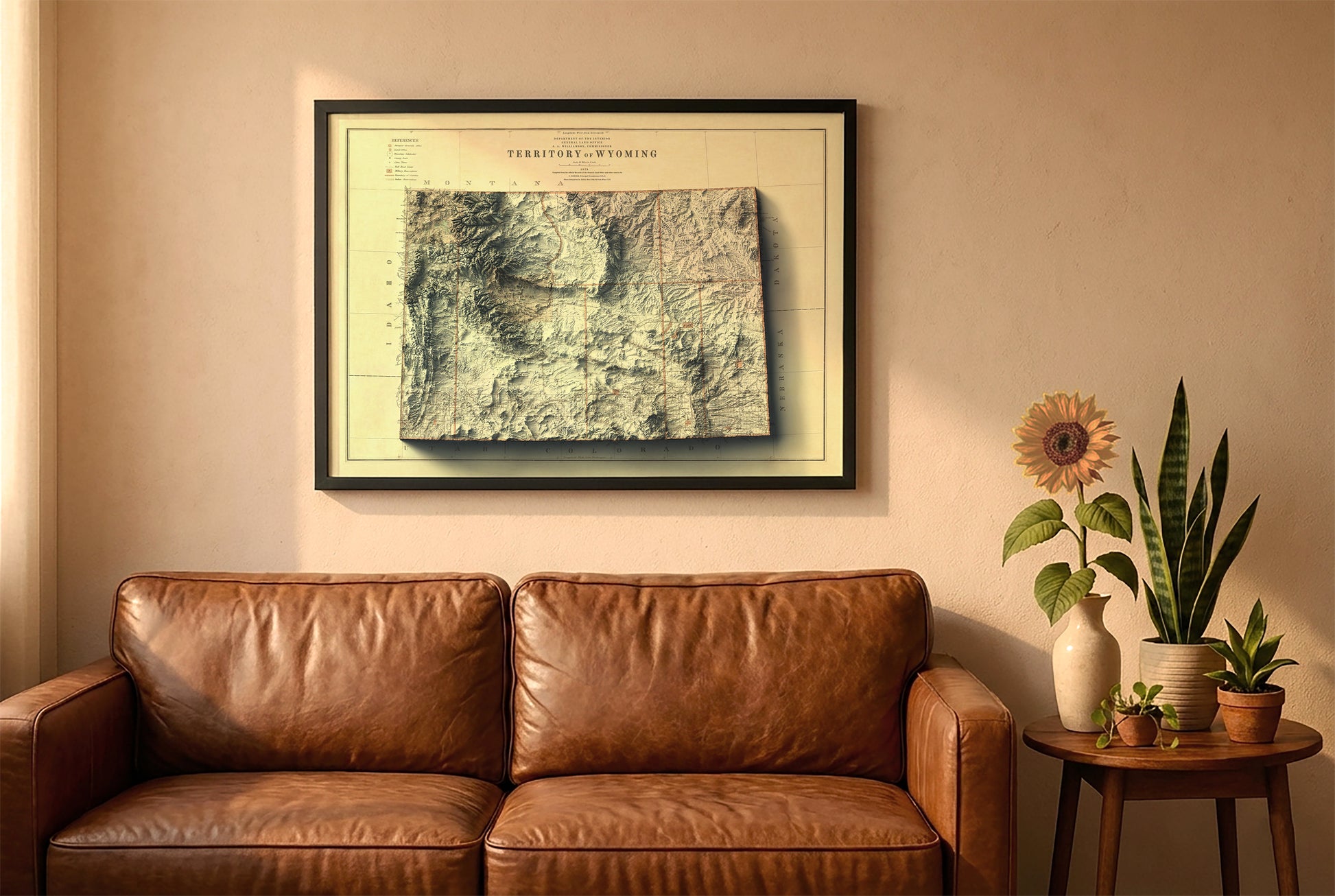 Wyoming vintage relief map in a black frame above a brown leather sofa. Boho living room with warm sunlight, sunflower, and indoor plants on a wooden side table