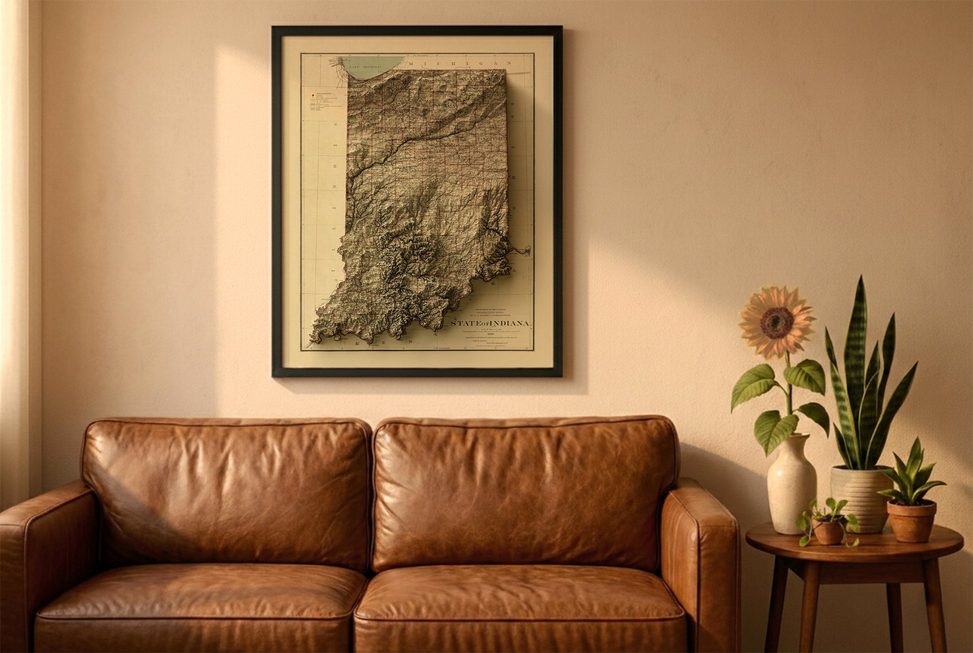 Indiana vintage relief map in a black frame above a brown leather sofa. Boho living room with warm sunlight, sunflower, and indoor plants on a wooden side table