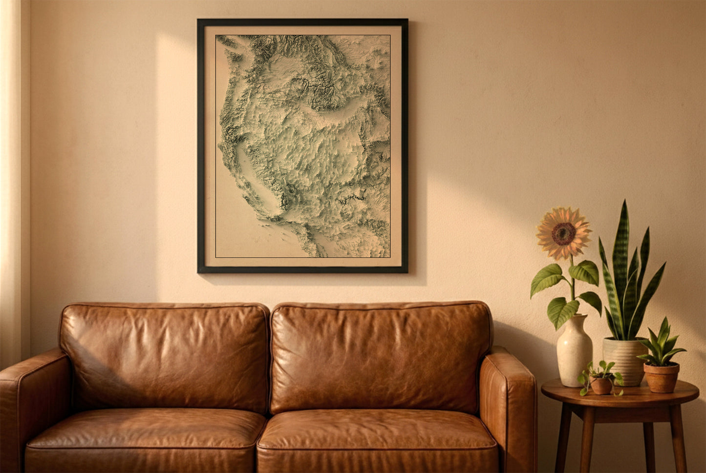 Western USA vintage relief map in a black frame above a brown leather sofa. Boho living room with warm sunlight, sunflower, and indoor plants on a wooden side table