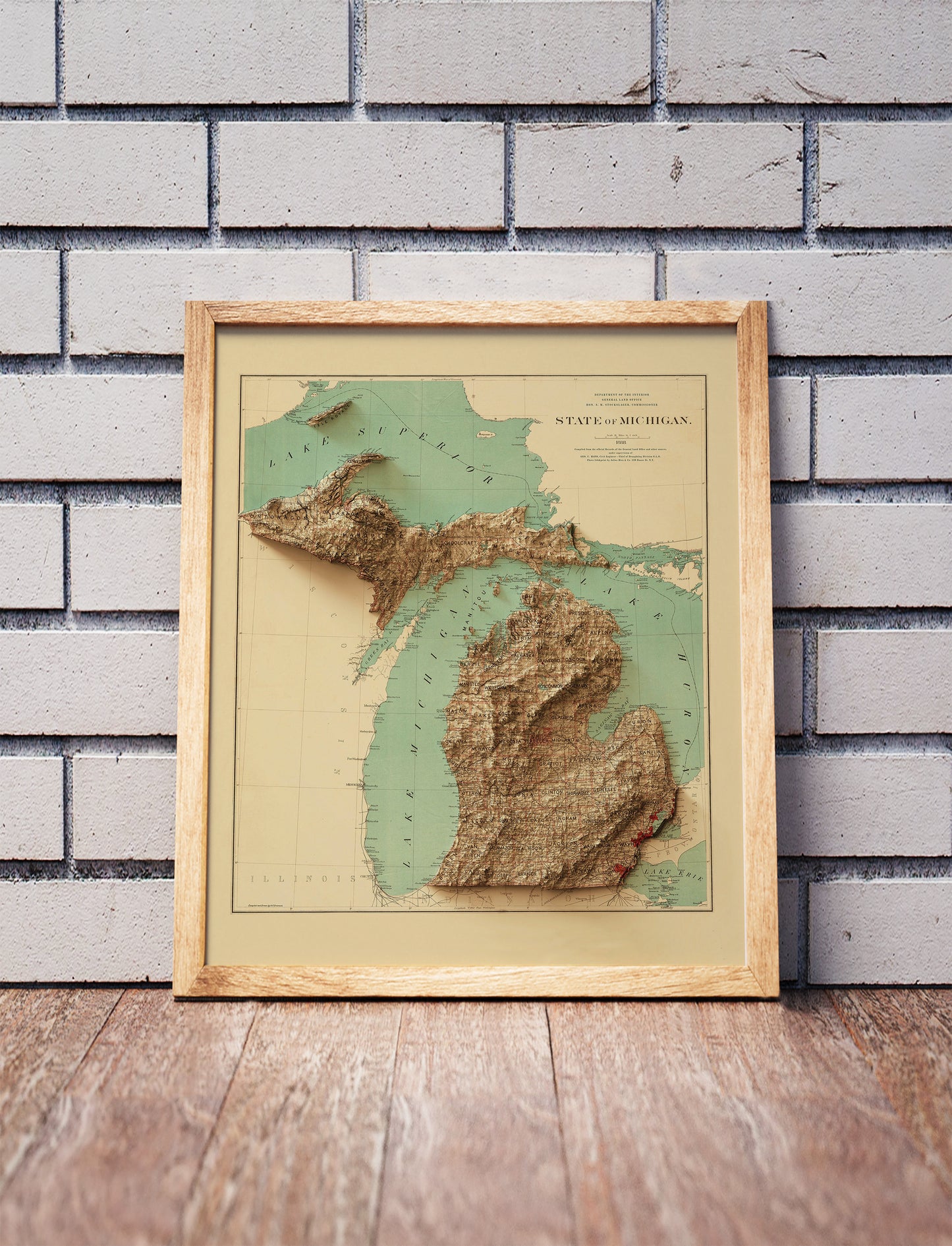 Vintage Michigan shaded relief map in a wooden frame. Realistic terrain art print for home decor, displayed against a brick wall
