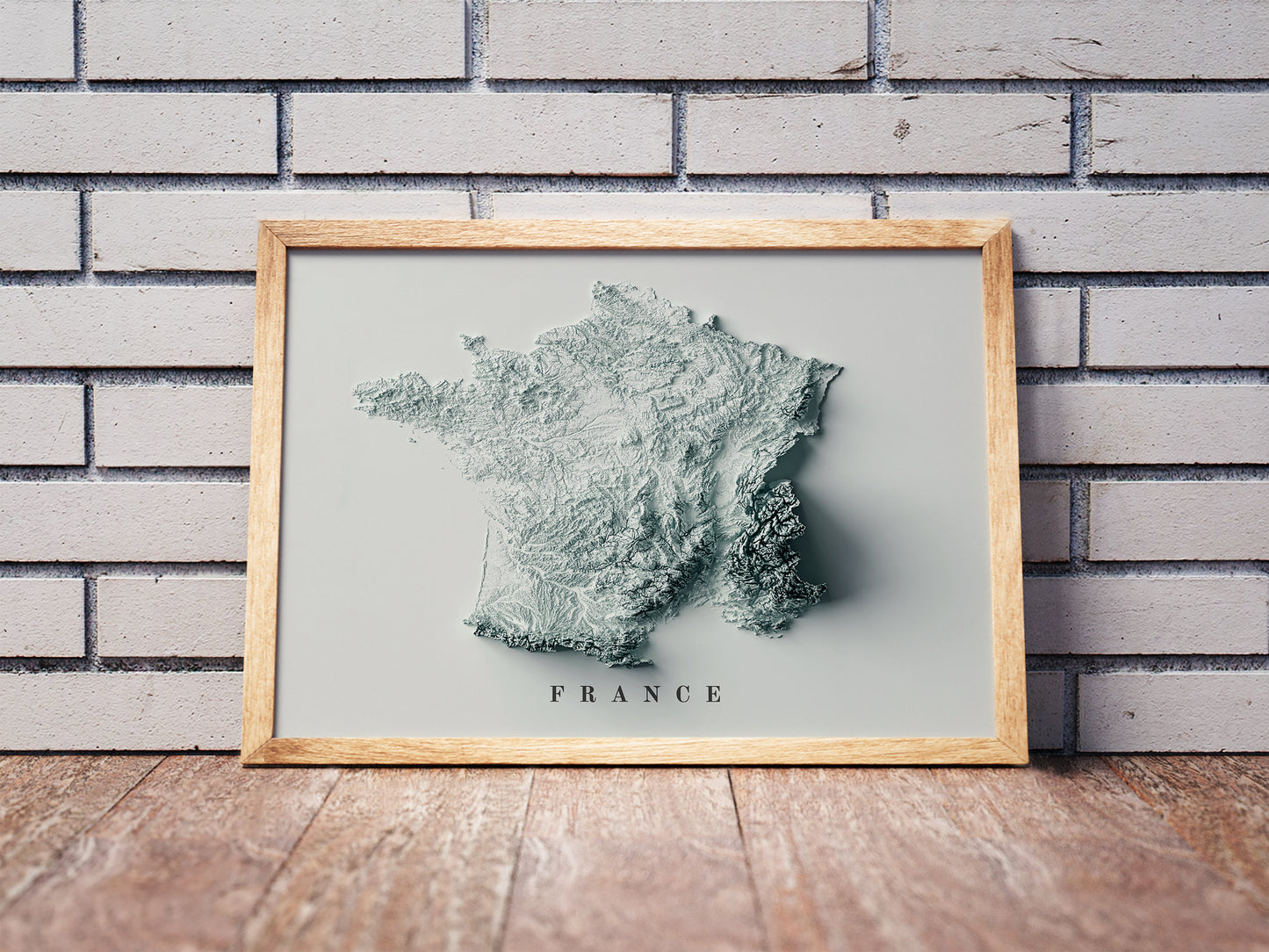 France shaded relief map in a wooden frame. Realistic terrain art print for home decor, displayed against a brick wall