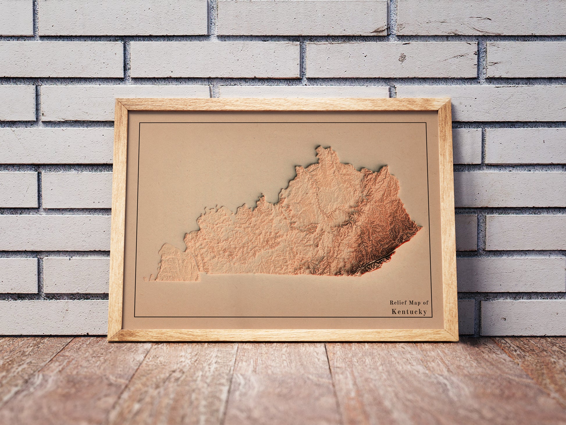 Vintage Kentucky shaded relief map in a wooden frame. Realistic terrain art print for home decor, displayed against a brick wall