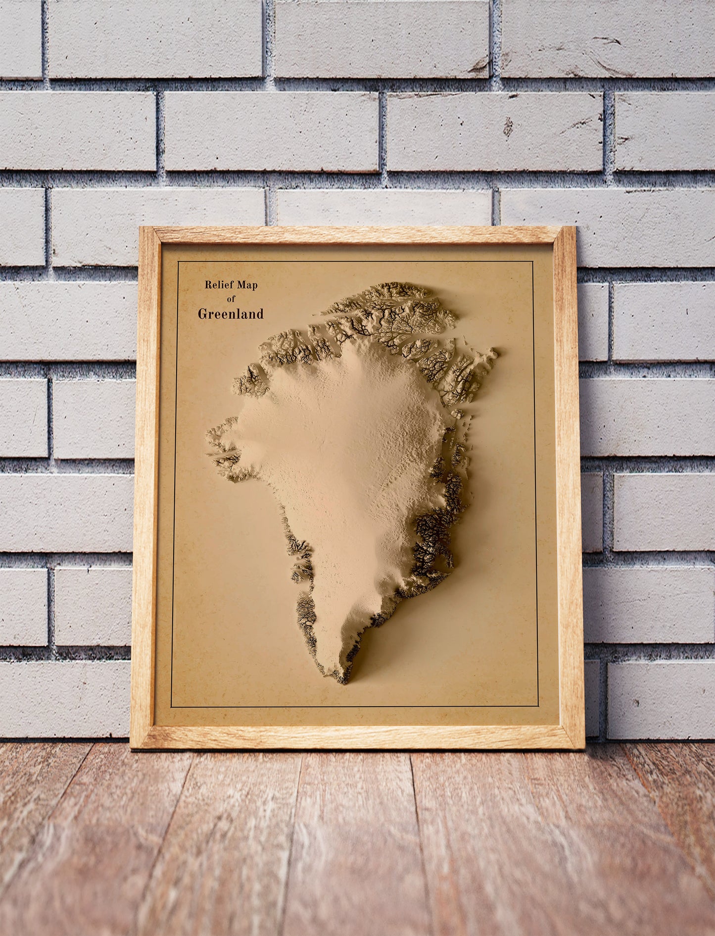 Vintage Greenland shaded relief map in a wooden frame. Realistic terrain art print for home decor, displayed against a brick wall