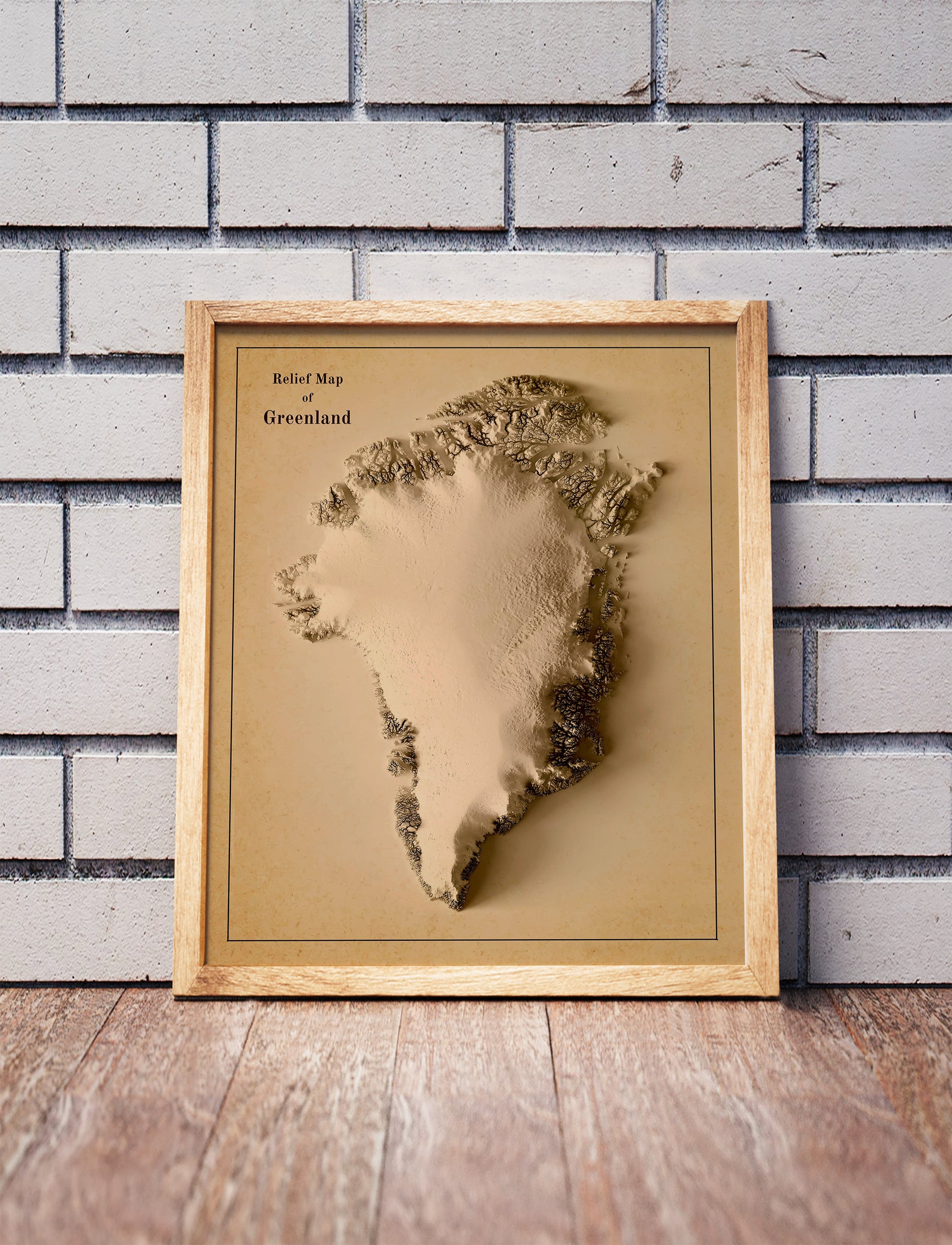 Vintage Greenland shaded relief map in a wooden frame. Realistic terrain art print for home decor, displayed against a brick wall