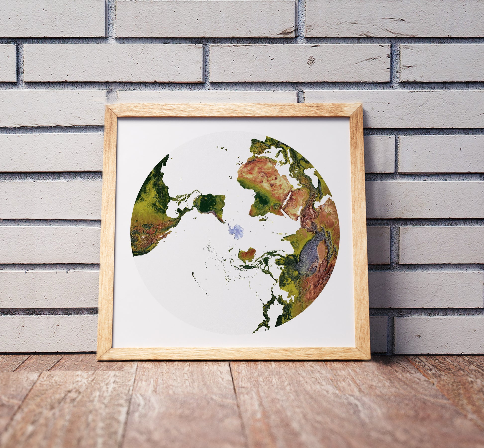 Australian Antarctic Polar projection shaded relief world map in a wooden frame. Realistic terrain art print for home decor, displayed against a brick wall