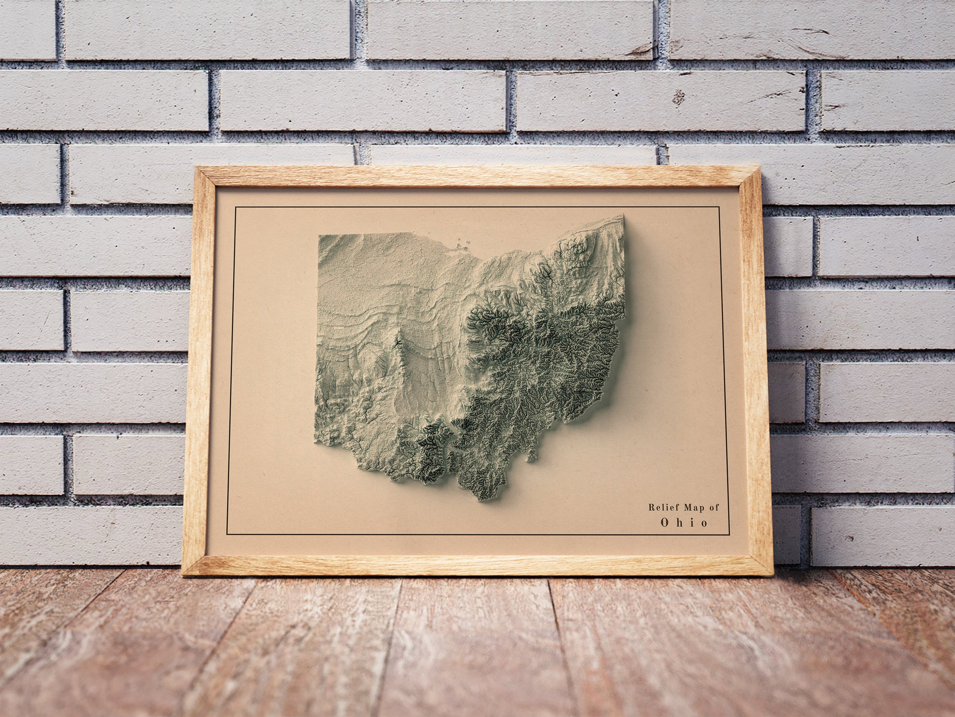 Vintage Ohio shaded relief map in a wooden frame. Realistic terrain art print for home decor, displayed against a brick wall