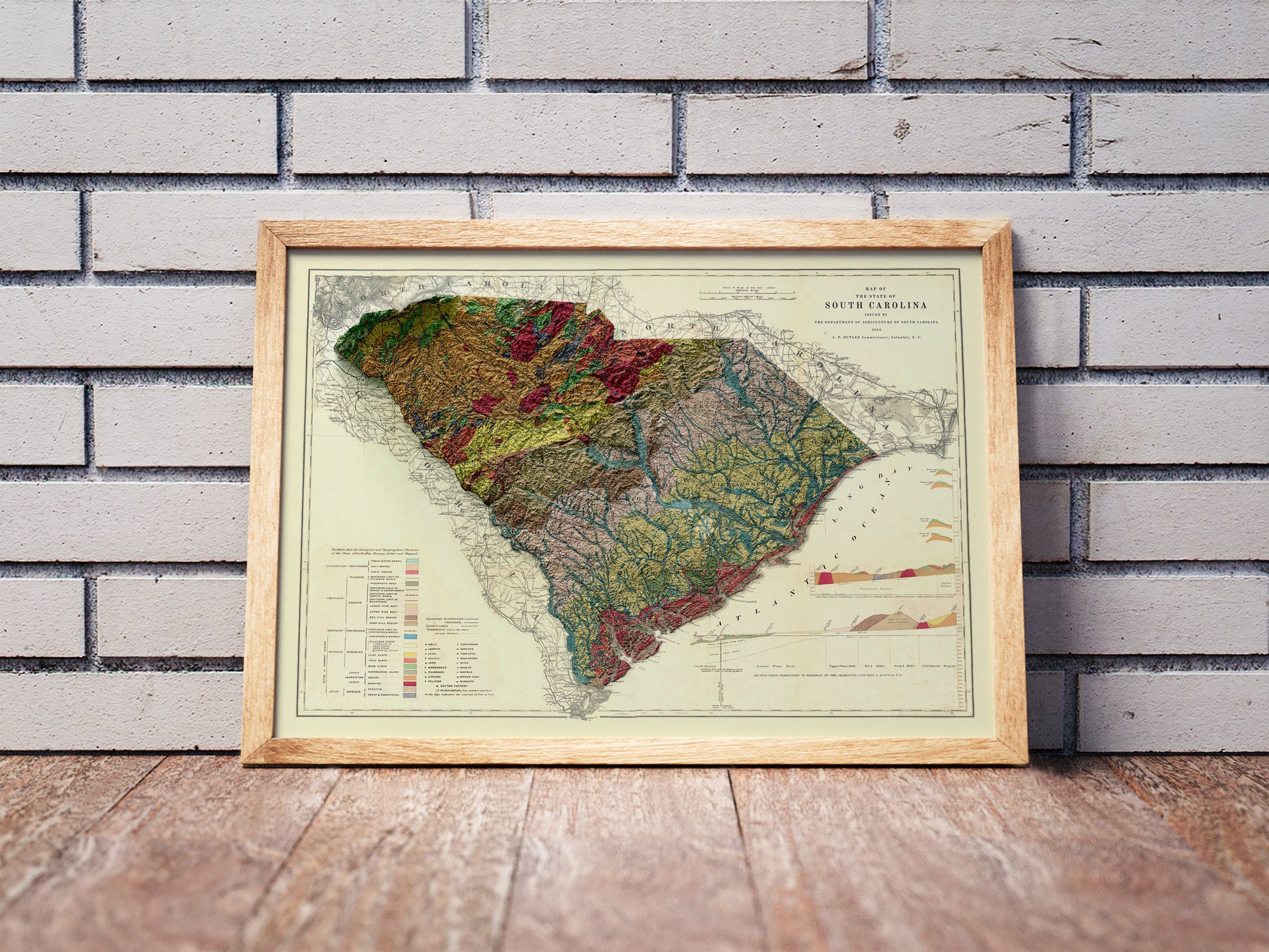 Vintage South Carolina shaded relief map in a wooden frame. Realistic terrain art print for home decor, displayed against a brick wall