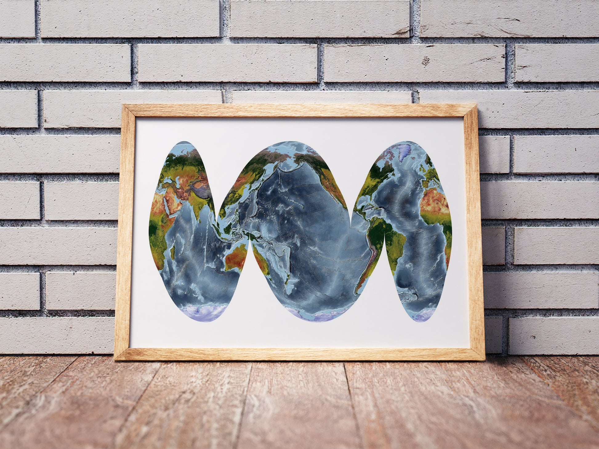 Goode Homolosine Ocean projection shaded relief world map in a wooden frame. Realistic terrain art print for home decor, displayed against a brick wall