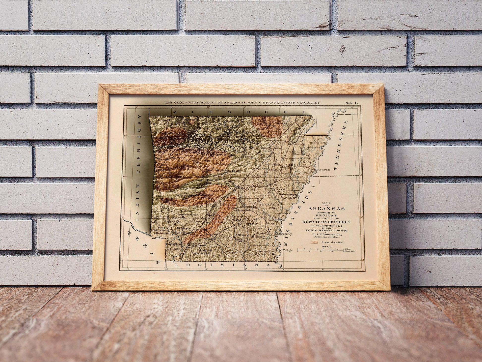 Vintage Arkansas shaded relief map in a wooden frame. Realistic terrain art print for home decor, displayed against a brick wall