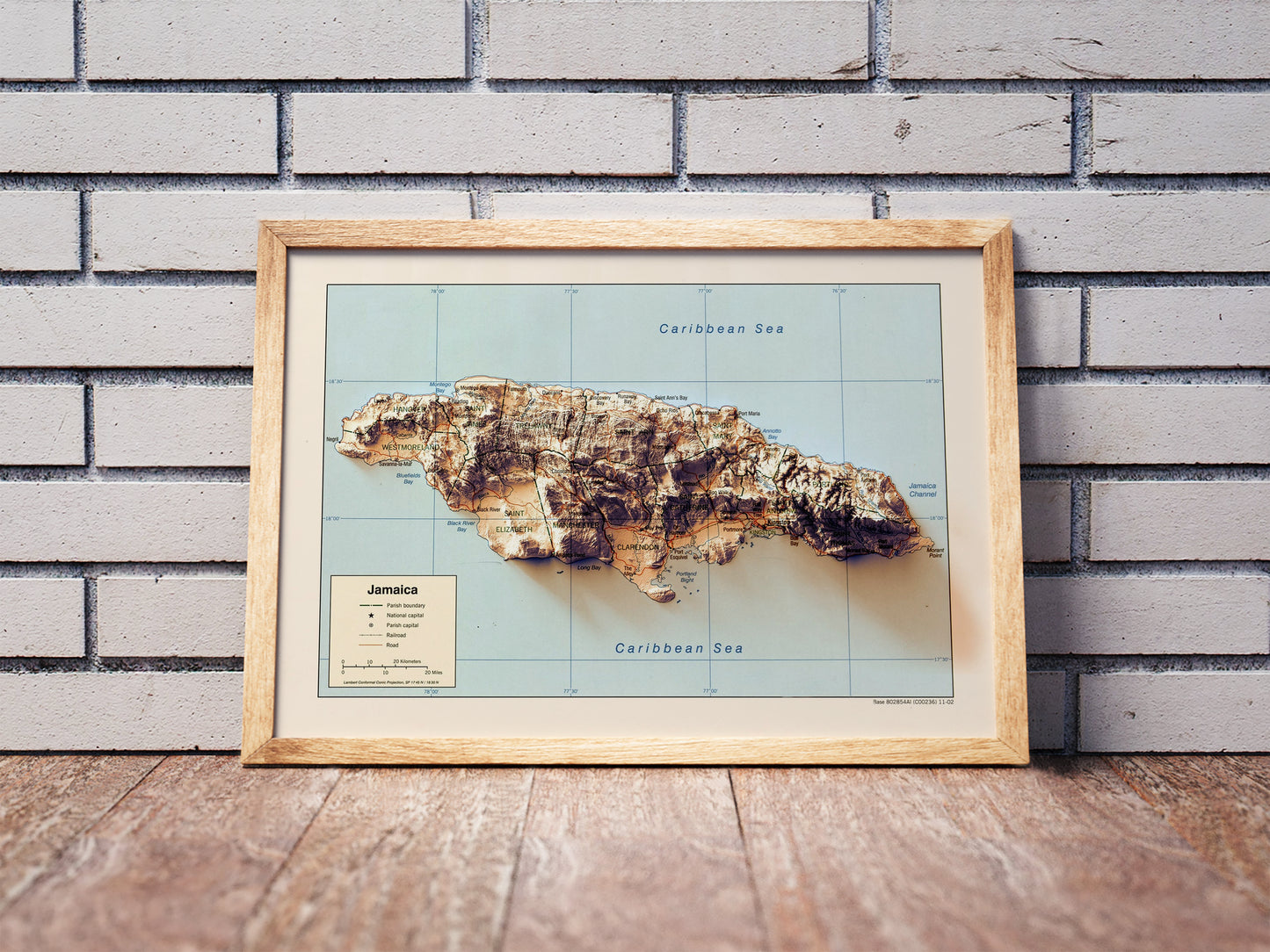 Vintage Jamaica shaded relief map in a wooden frame. Realistic terrain art print for home decor, displayed against a brick wall