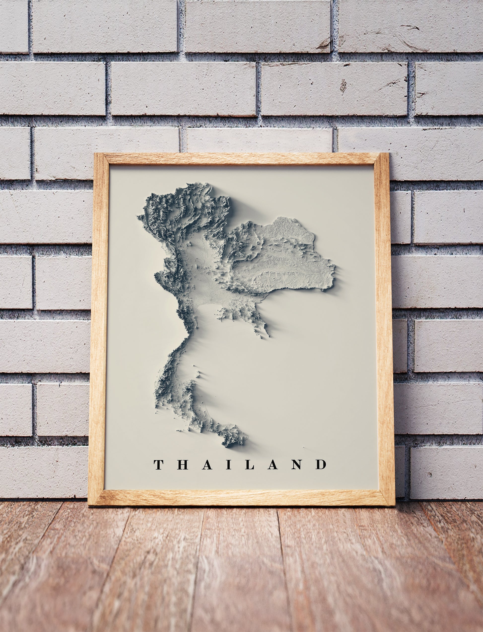 Thailand shaded relief map in a wooden frame. Realistic terrain art print for home decor, displayed against a brick wall