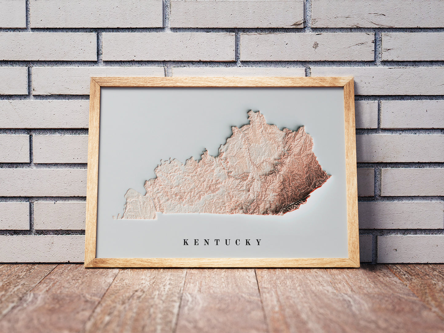 Kentucky shaded relief map in a wooden frame. Realistic terrain art print for home decor, displayed against a brick wall