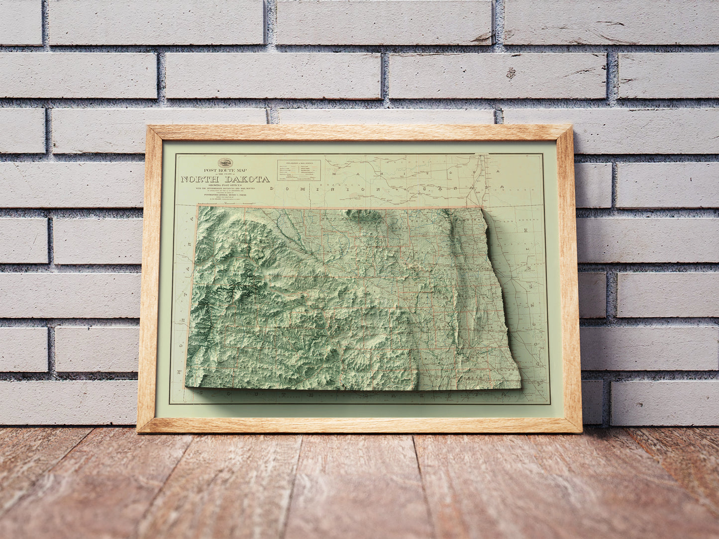 Vintage North Dakota shaded relief map in a wooden frame. Realistic terrain art print for home decor, displayed against a brick wall