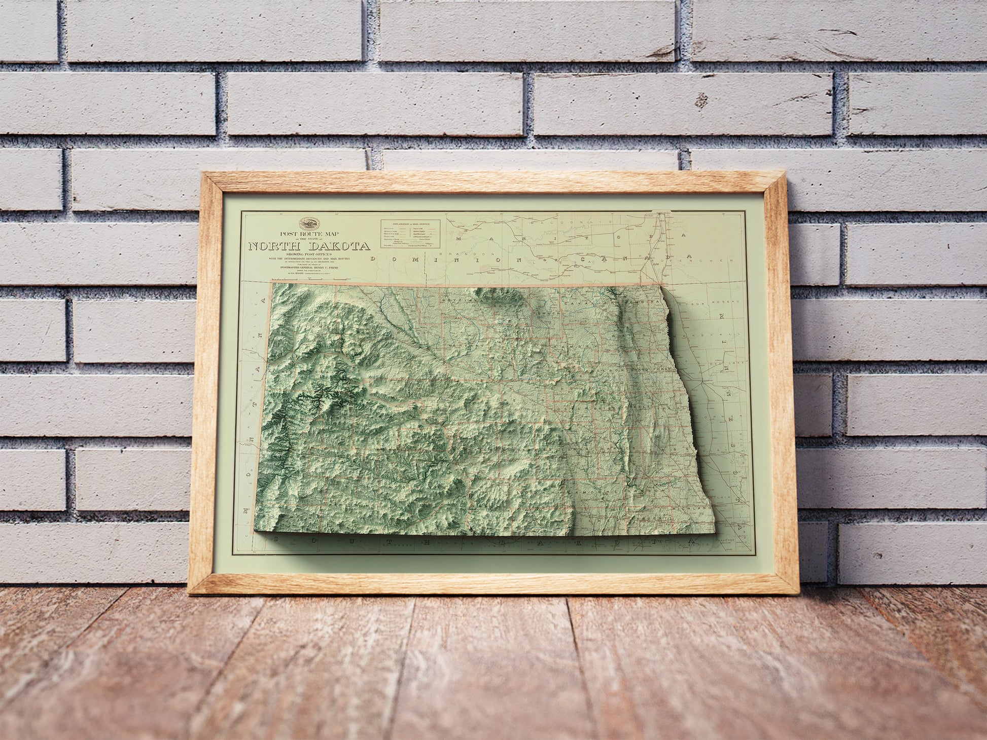 Vintage North Dakota shaded relief map in a wooden frame. Realistic terrain art print for home decor, displayed against a brick wall