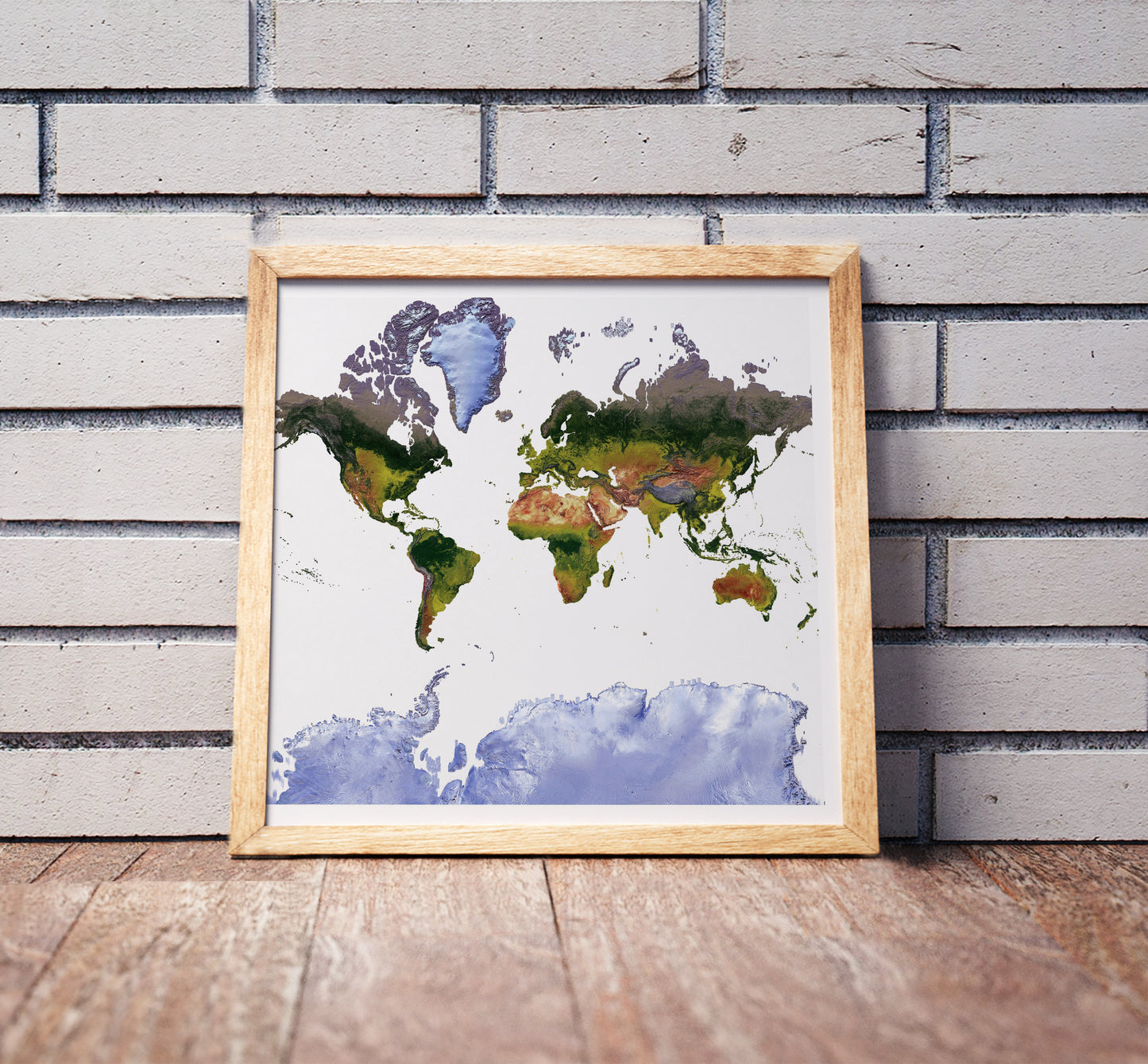 Mercator projection shaded relief world map in a wooden frame. Realistic terrain art print for home decor, displayed against a brick wall