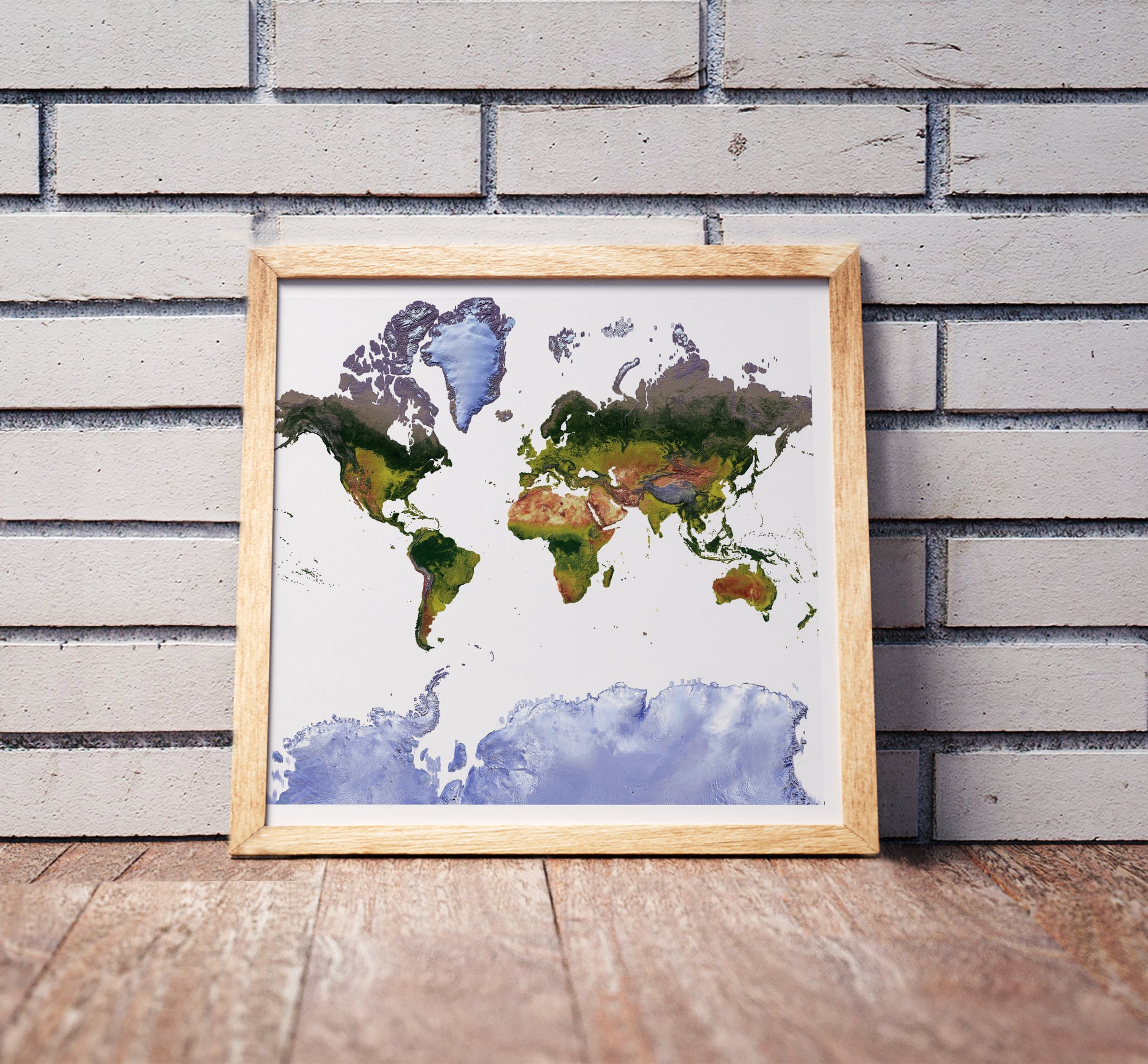 Mercator projection shaded relief world map in a wooden frame. Realistic terrain art print for home decor, displayed against a brick wall