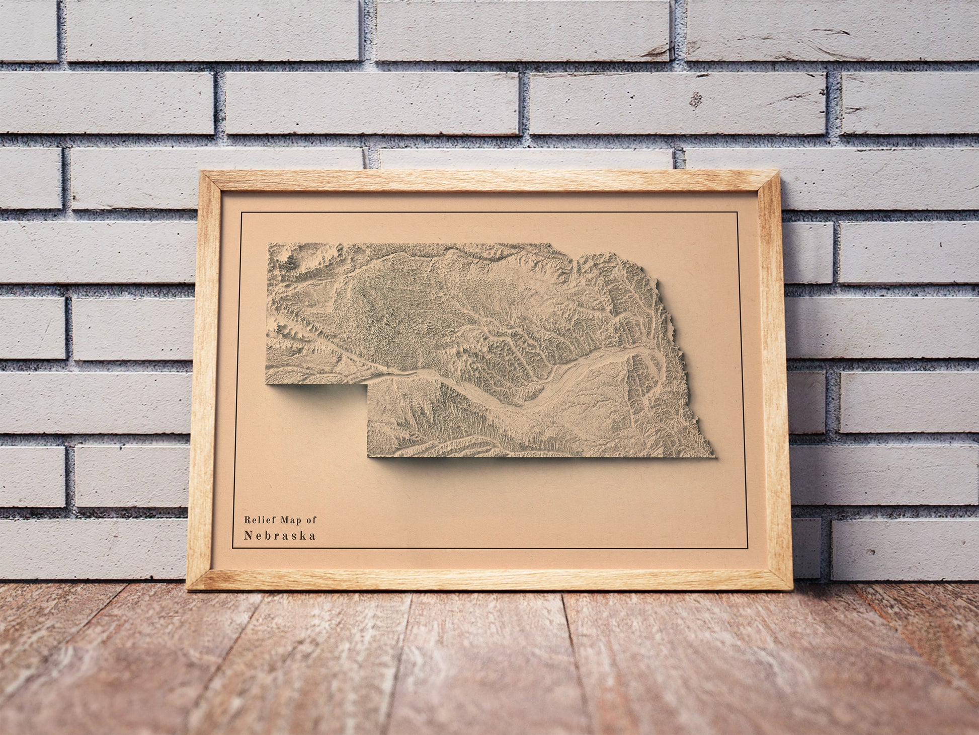 Vintage Nebraska shaded relief map in a wooden frame. Realistic terrain art print for home decor, displayed against a brick wall