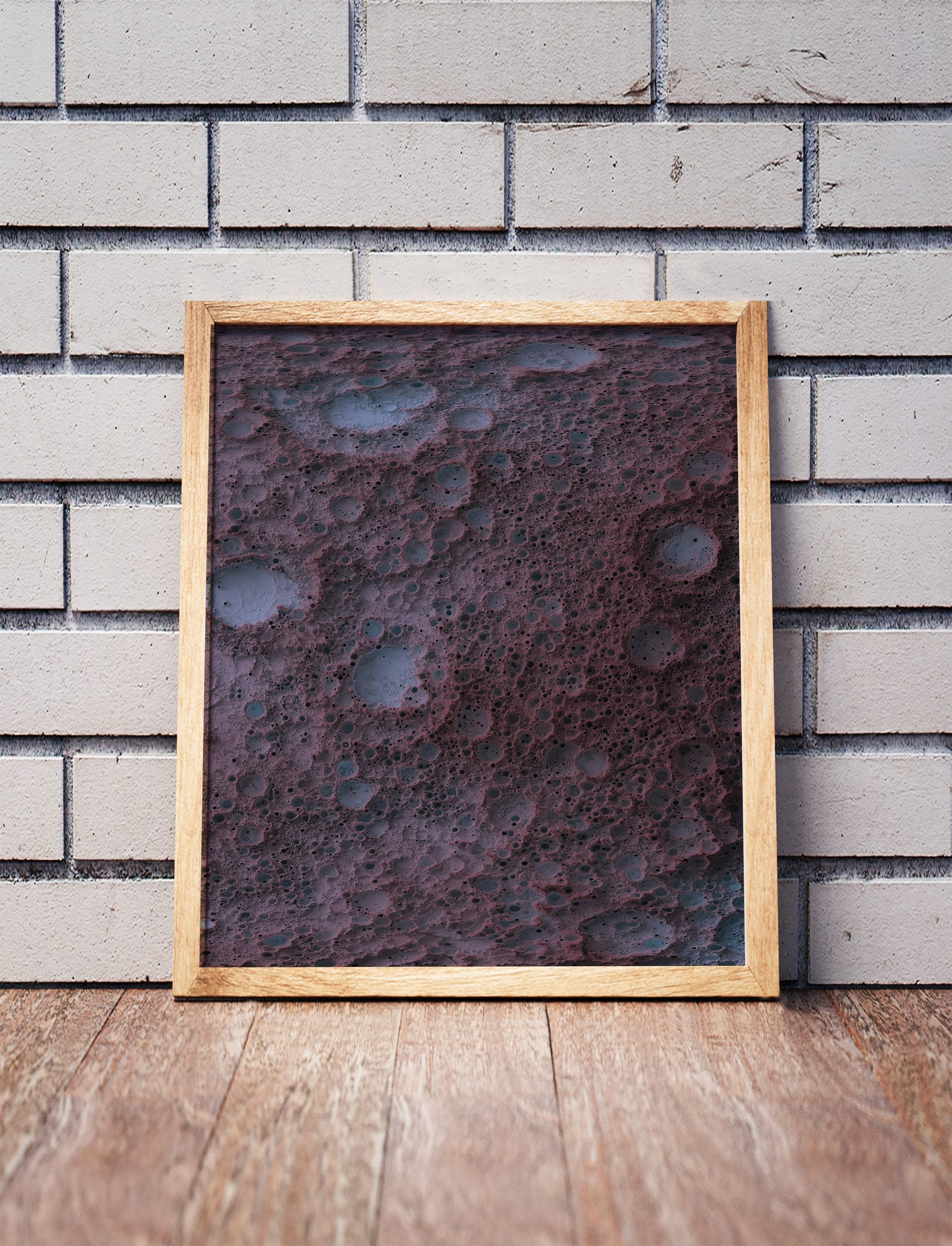 Moon shaded relief map in a wooden frame. Realistic terrain art print for home decor, displayed against a brick wall