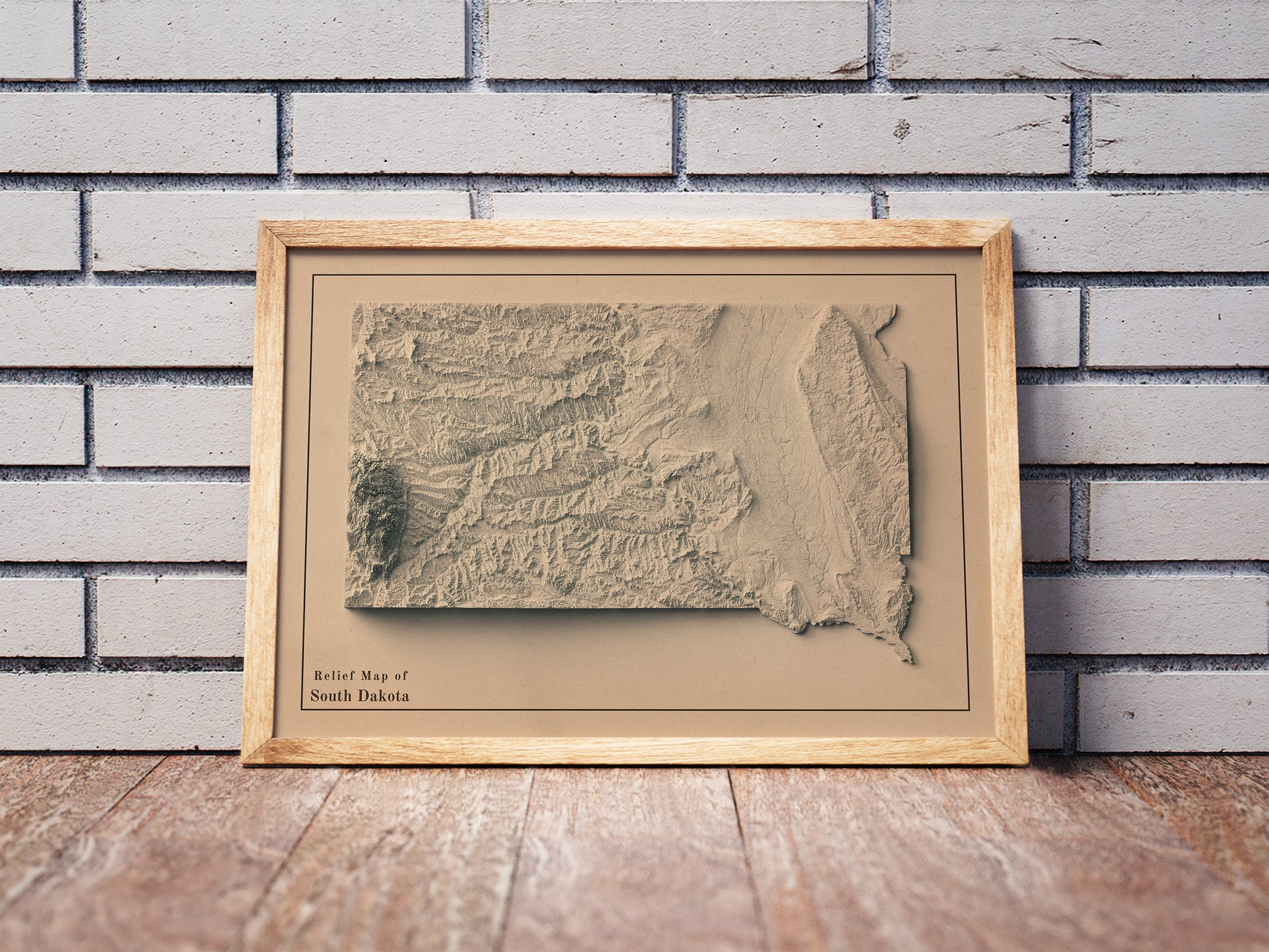 Vintage South Dakota shaded relief map in a wooden frame. Realistic terrain art print for home decor, displayed against a brick wall