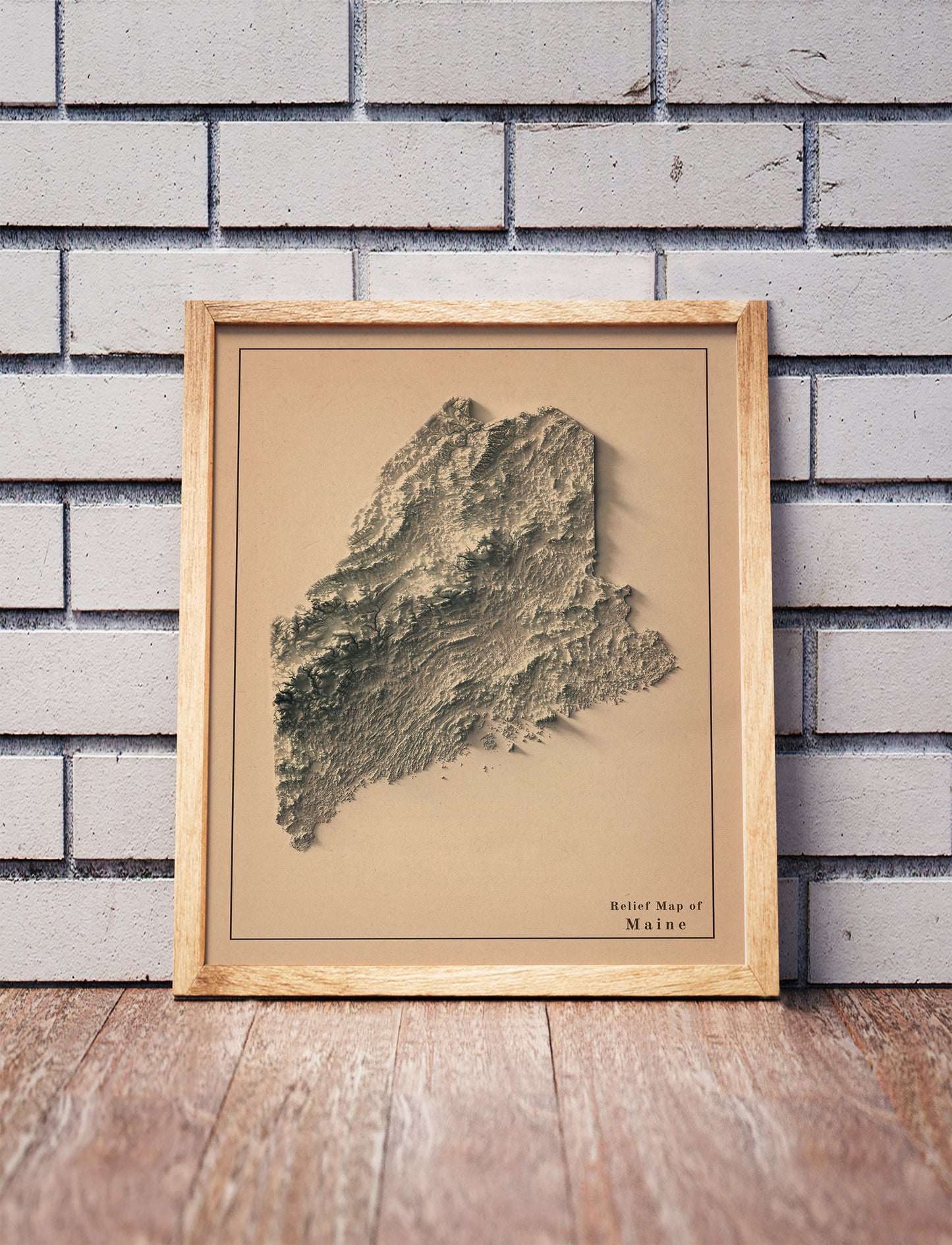 Vintage Maine shaded relief map in a wooden frame. Realistic terrain art print for home decor, displayed against a brick wall