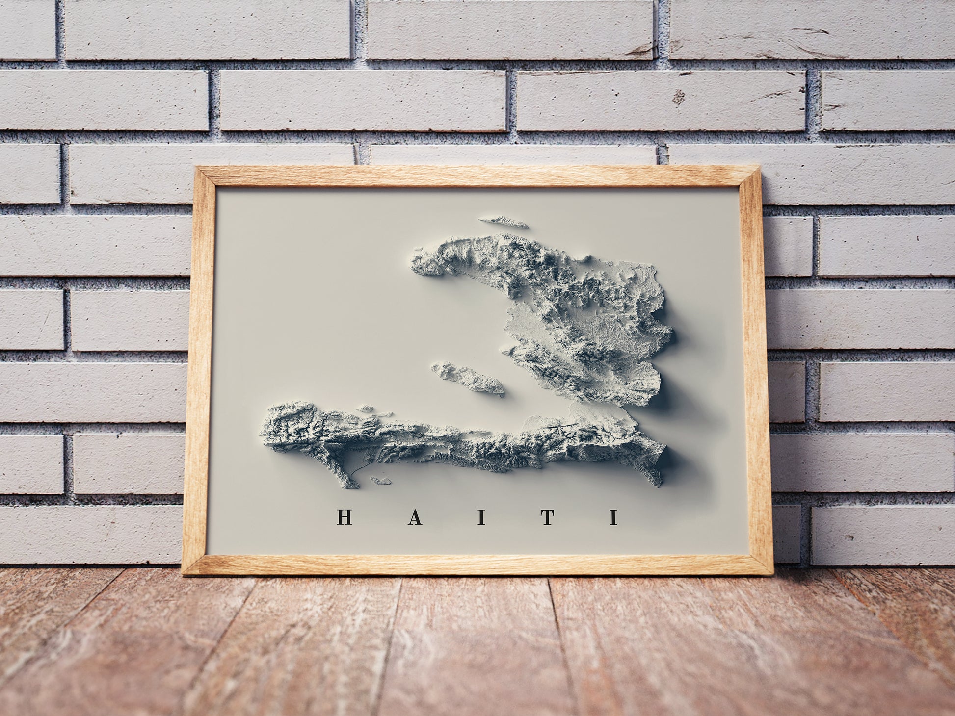 Haiti shaded relief map in a wooden frame. Realistic terrain art print for home decor, displayed against a brick wall