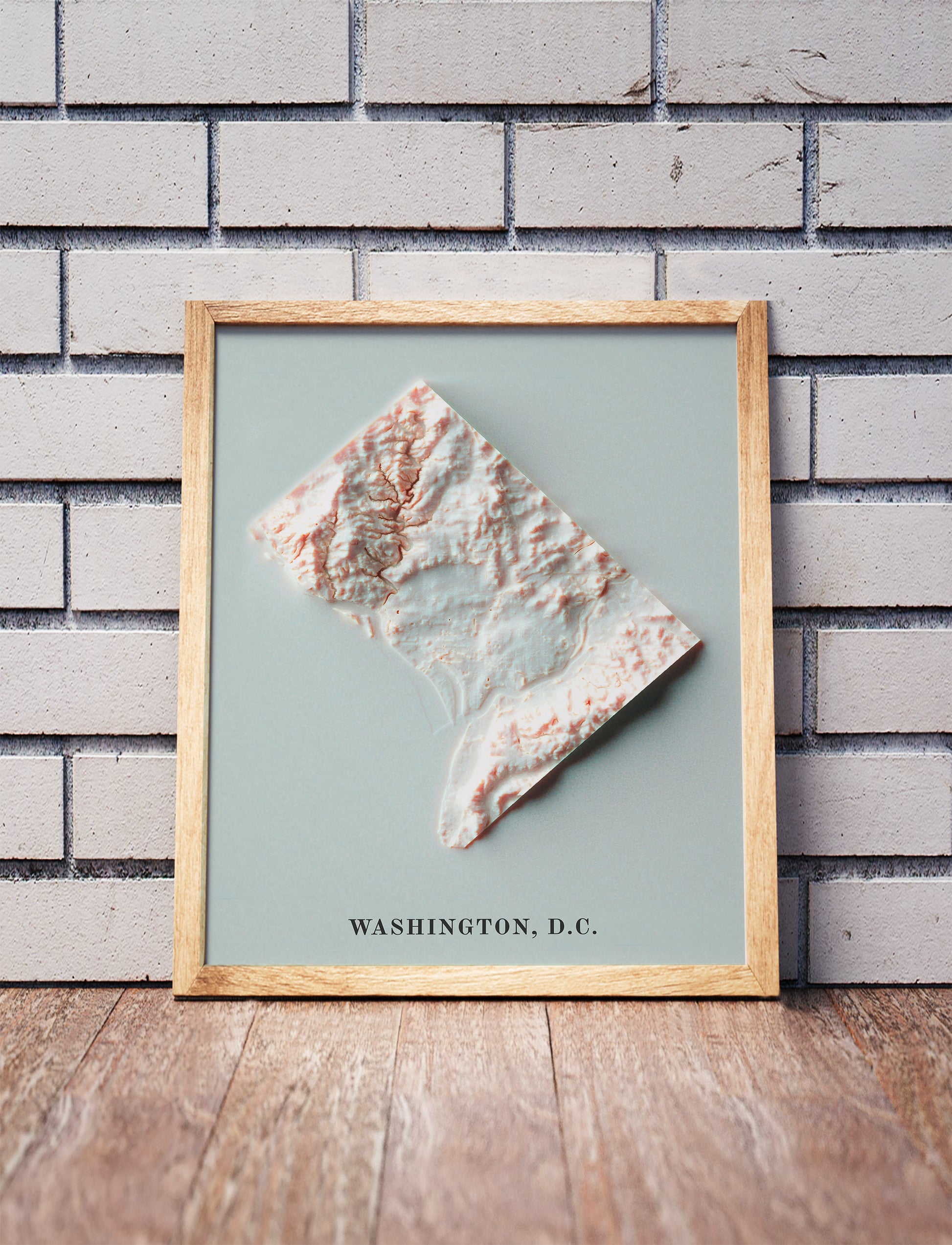 Washington DC shaded relief map in a wooden frame. Realistic terrain art print for home decor, displayed against a brick wall