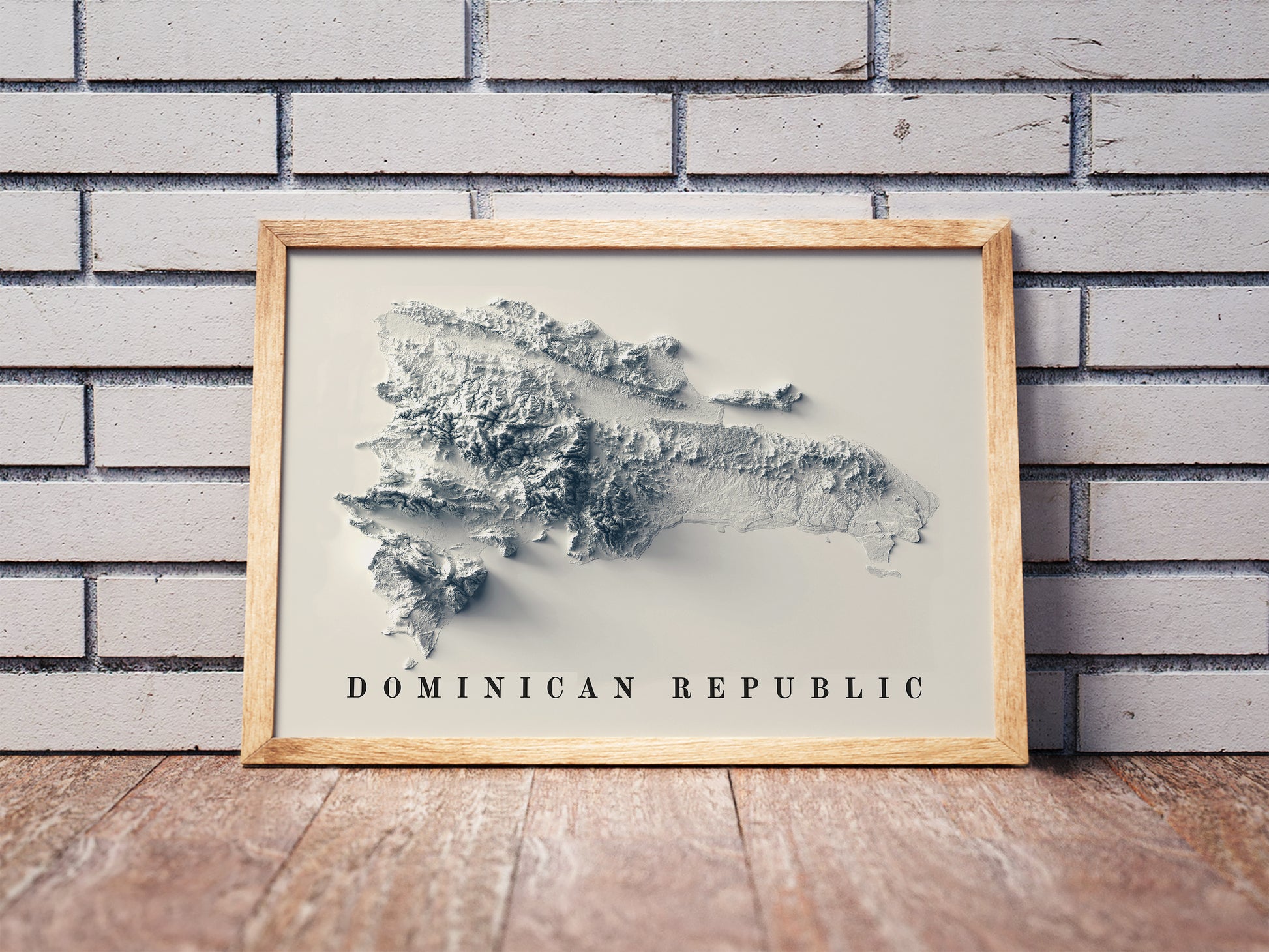 Dominican Republic shaded relief map in a wooden frame. Realistic terrain art print for home decor, displayed against a brick wall