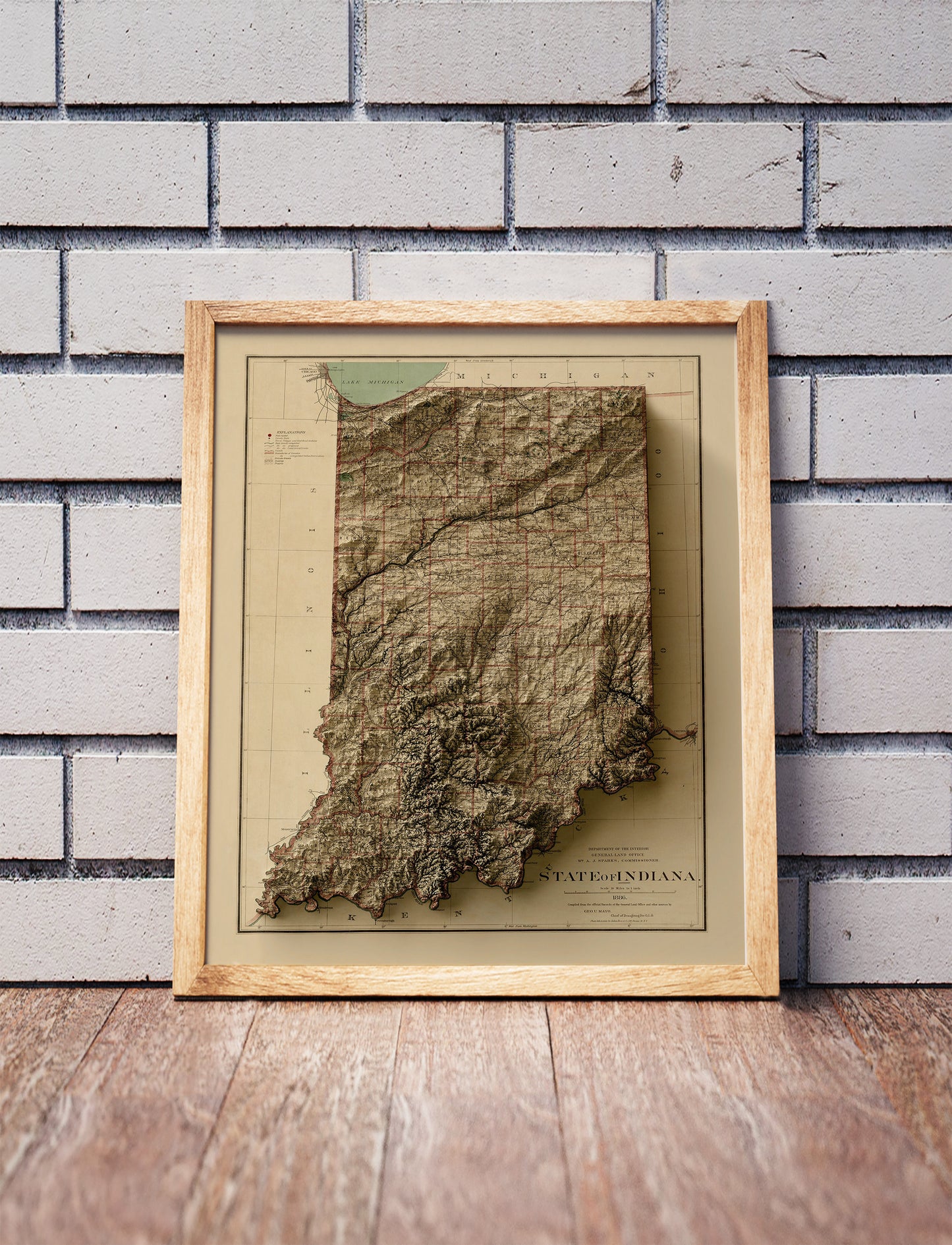 Vintage Indiana shaded relief map in a wooden frame. Realistic terrain art print for home decor, displayed against a brick wall