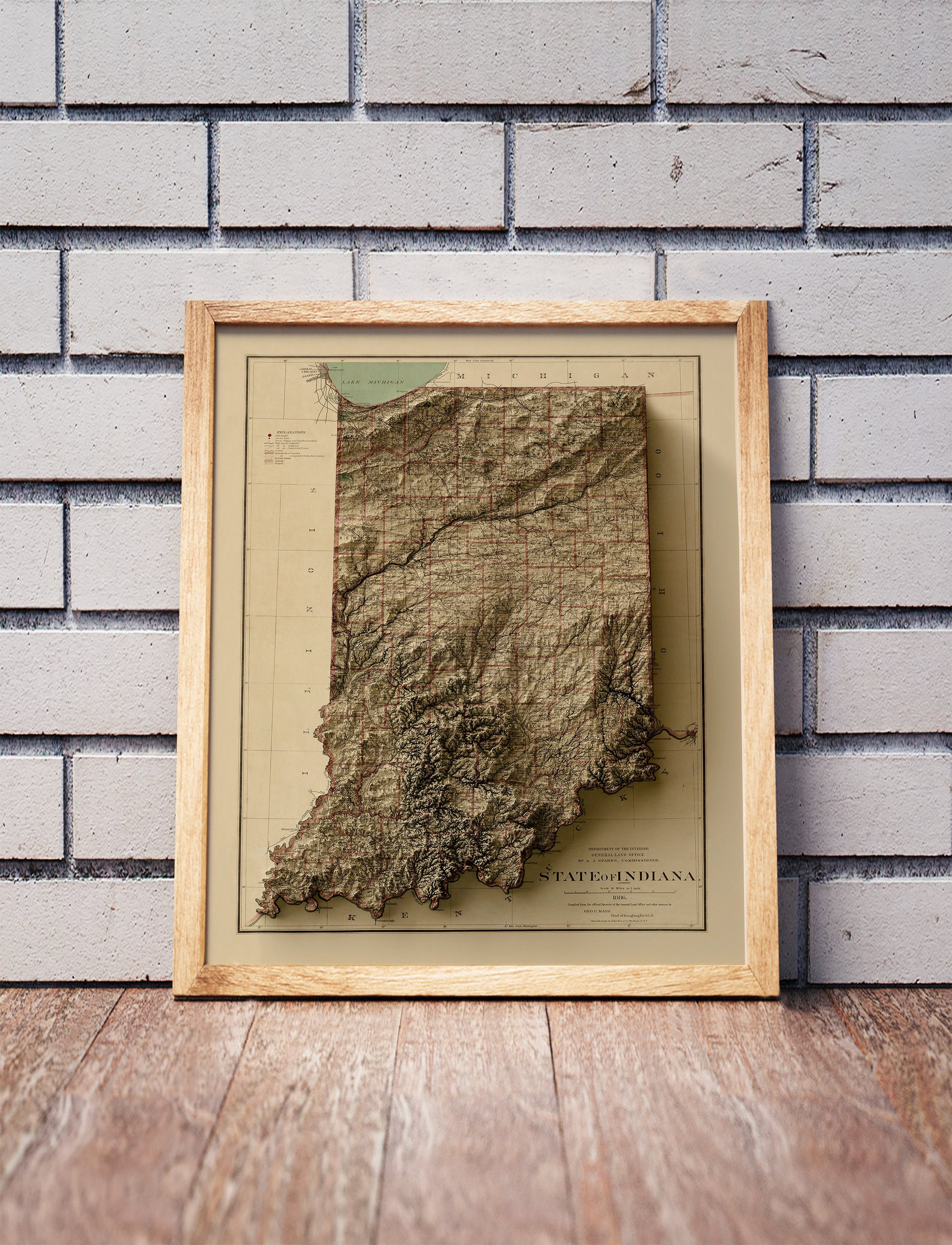 Vintage Indiana shaded relief map in a wooden frame. Realistic terrain art print for home decor, displayed against a brick wall