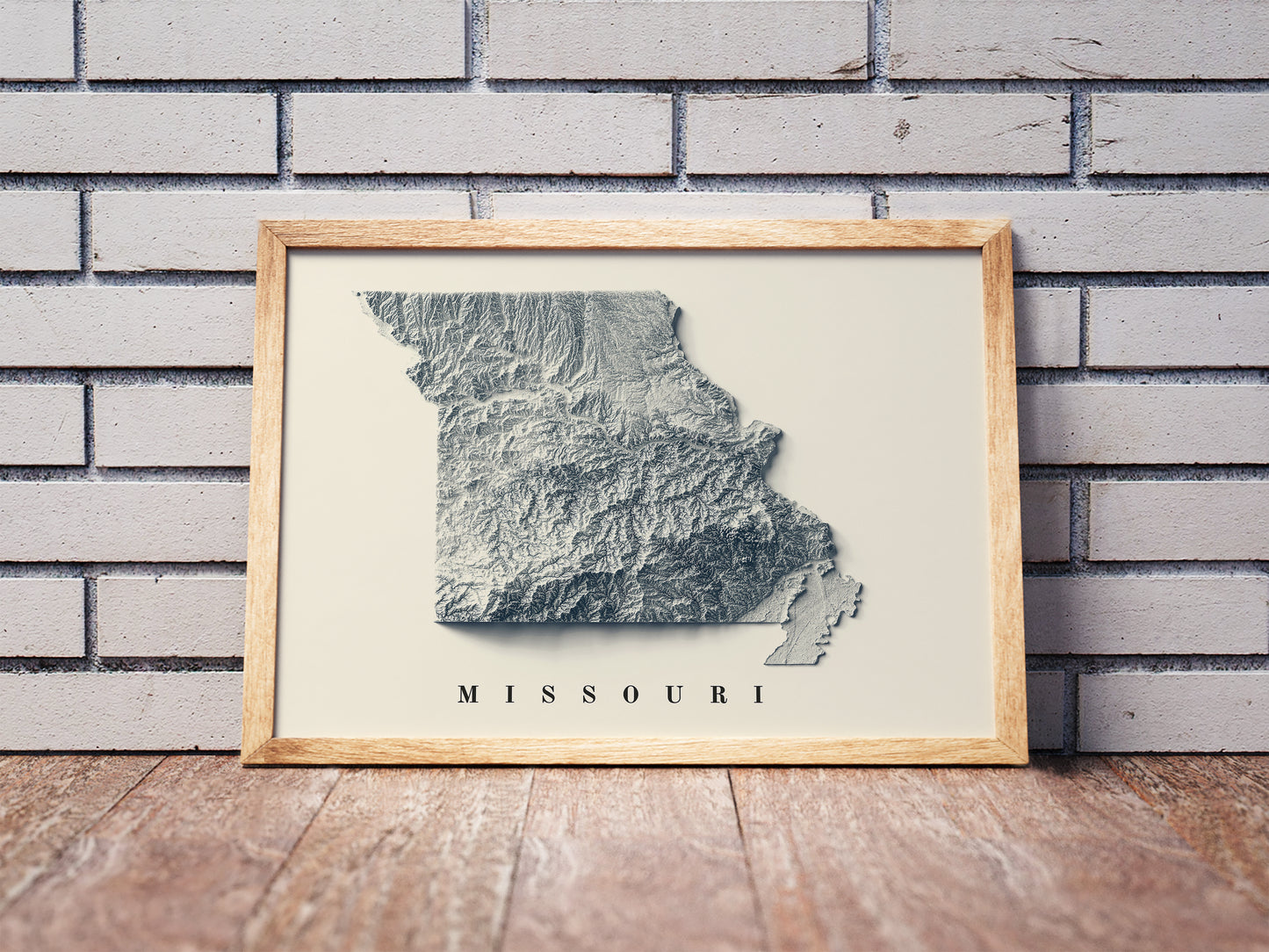 Missouri shaded relief map in a wooden frame. Realistic terrain art print for home decor, displayed against a brick wall