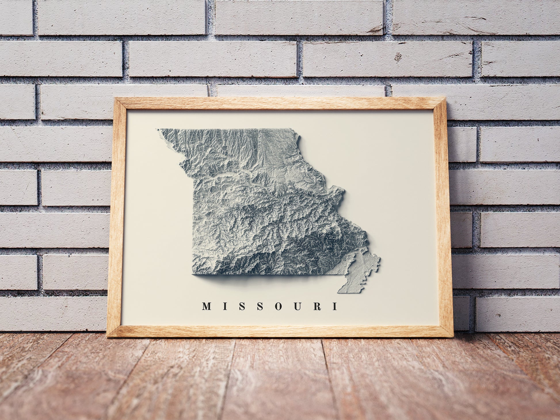 Missouri shaded relief map in a wooden frame. Realistic terrain art print for home decor, displayed against a brick wall