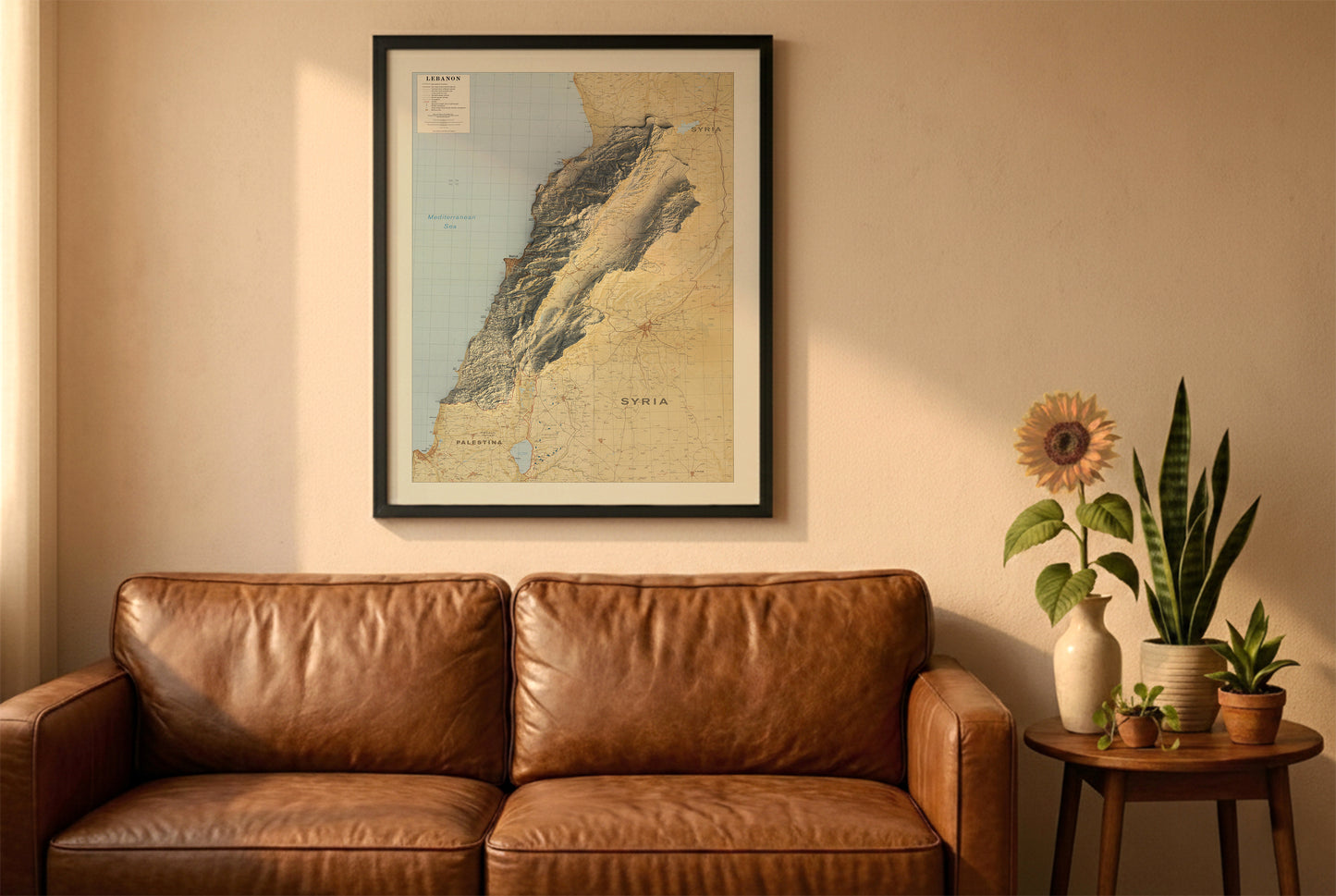 Lebanon vintage relief map in a black frame above a brown leather sofa. Boho living room with warm sunlight, sunflower, and indoor plants on a wooden side table