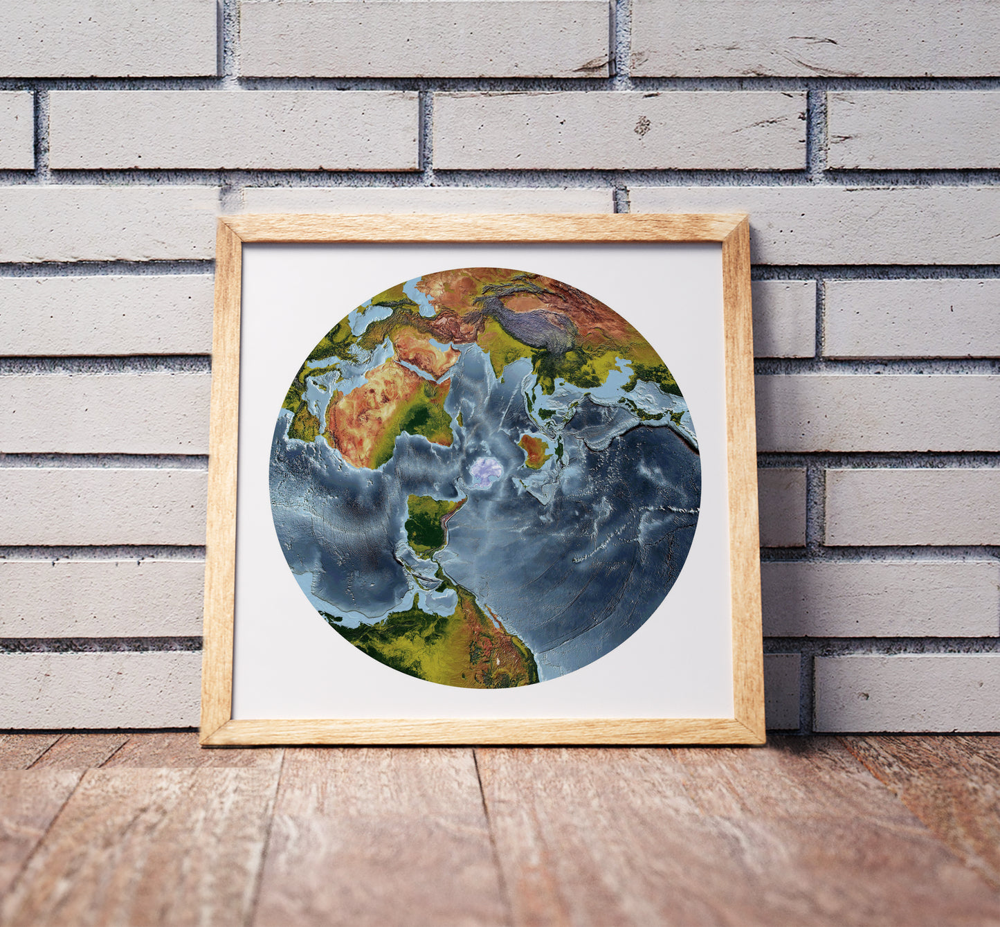 Australian Antarctic Polar projection shaded relief world map in a wooden frame. Realistic terrain art print for home decor, displayed against a brick wall