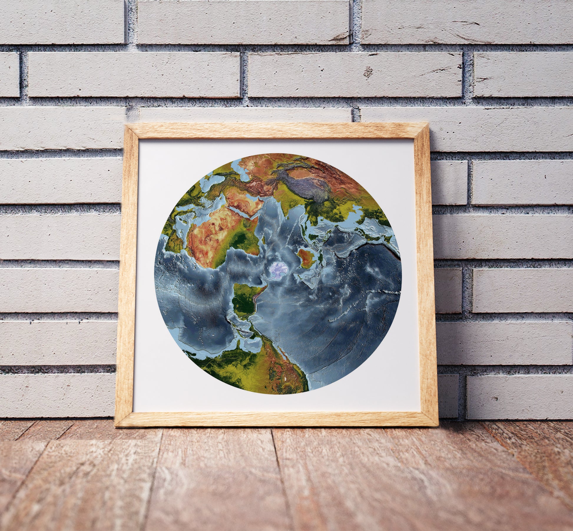 Australian Antarctic Polar projection shaded relief world map in a wooden frame. Realistic terrain art print for home decor, displayed against a brick wall
