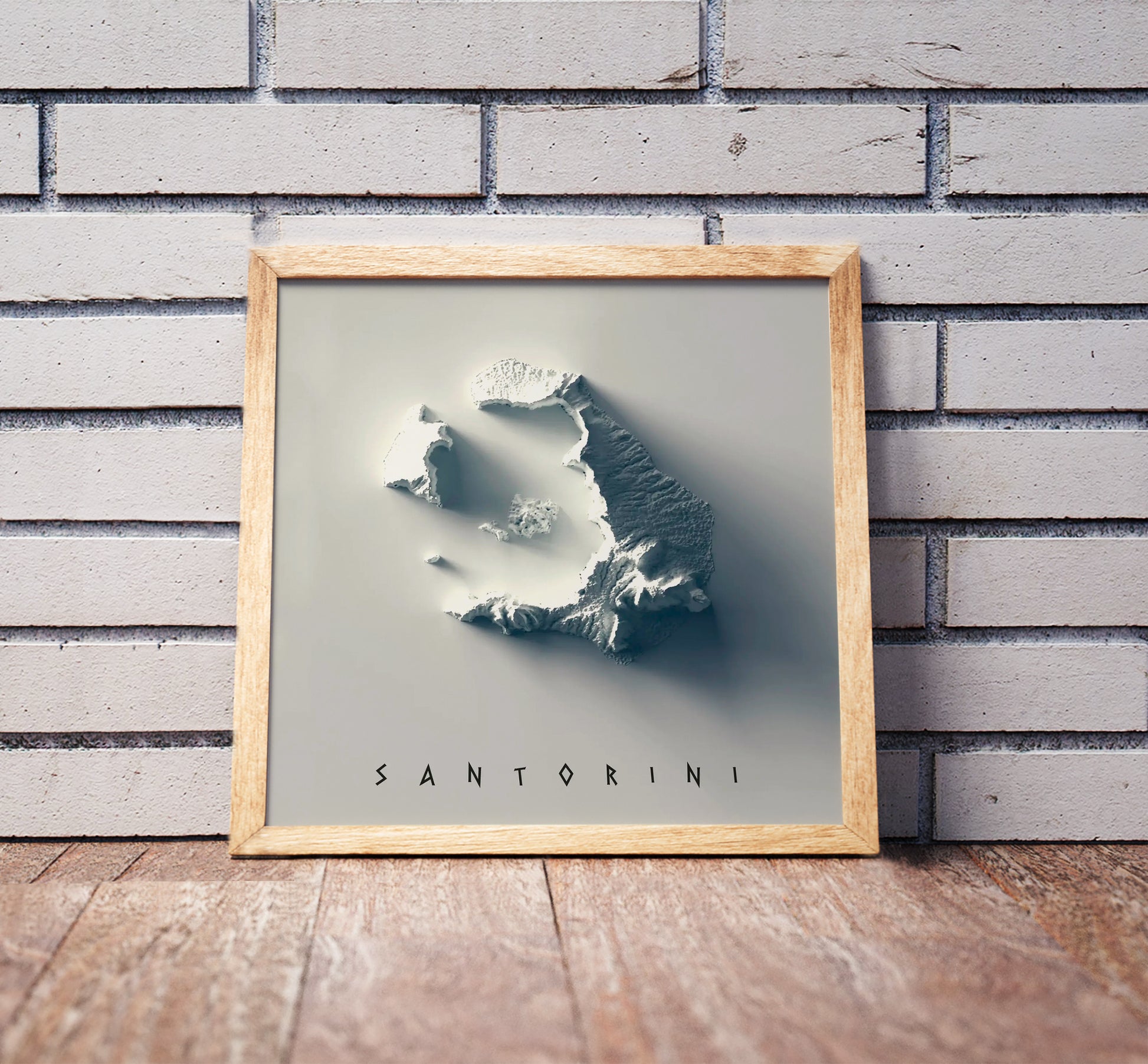 Santorini, Greece, shaded relief map in a wooden frame. Realistic terrain art print for home decor, displayed against a brick wall
