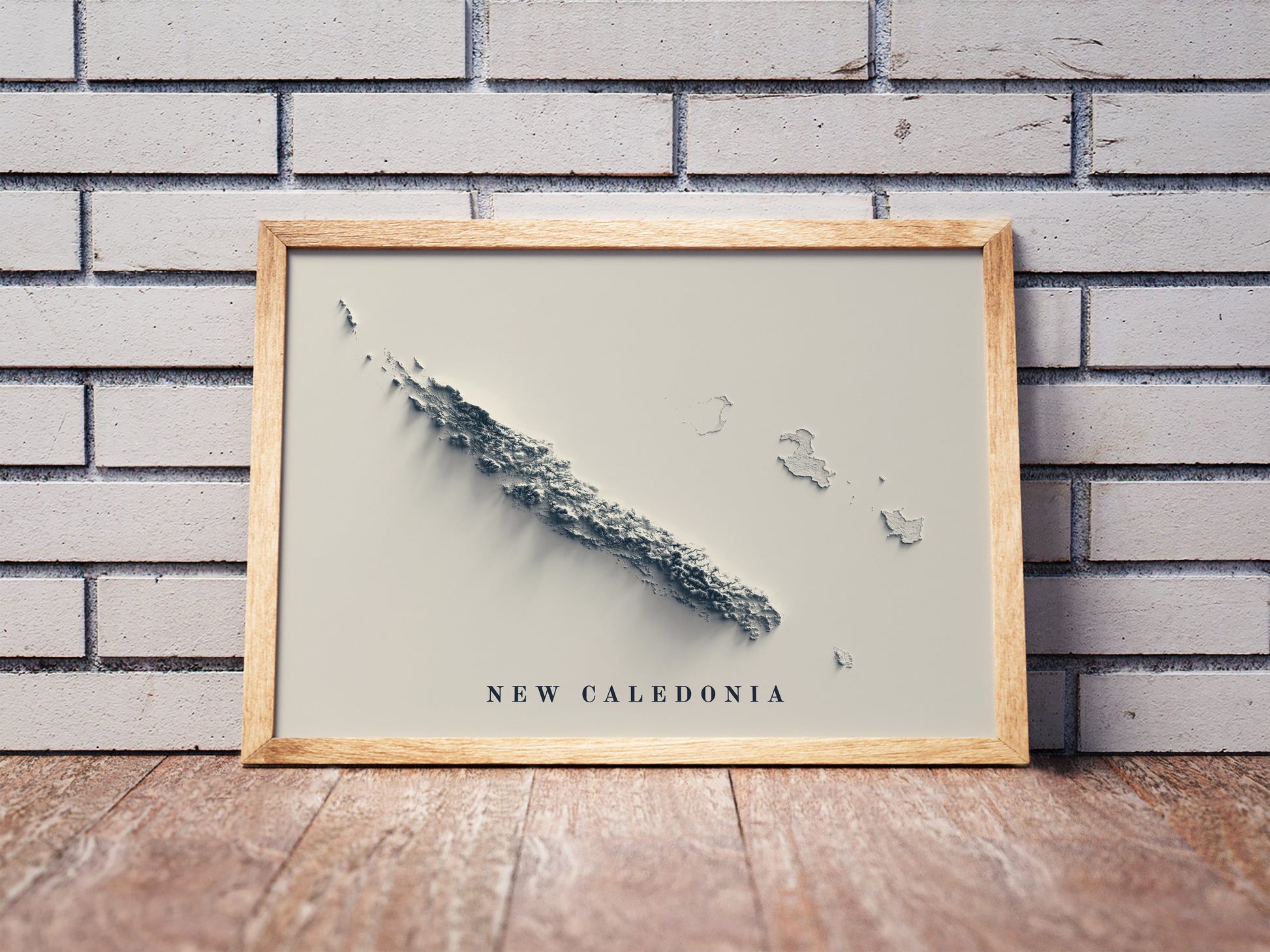 New Caledonia shaded relief map in a wooden frame. Realistic terrain art print for home decor, displayed against a brick wall