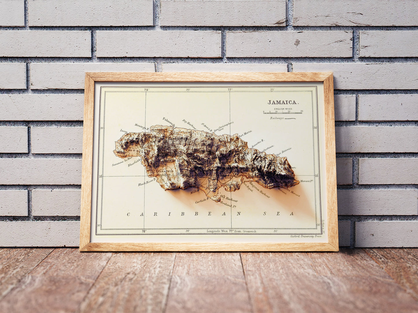 Vintage Jamaica shaded relief map in a wooden frame. Realistic terrain art print for home decor, displayed against a brick wall