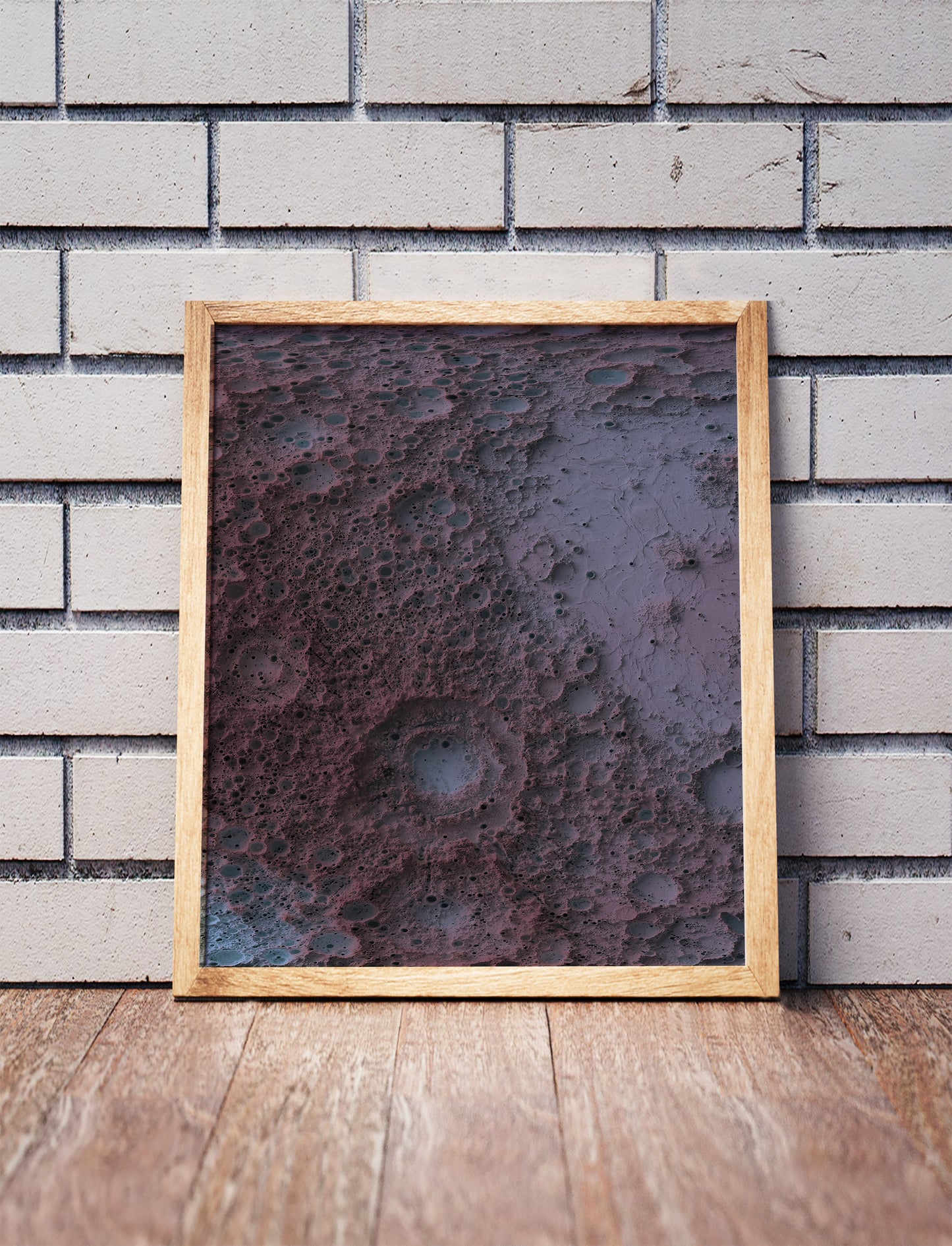 Moon shaded relief map in a wooden frame. Realistic terrain art print for home decor, displayed against a brick wall
