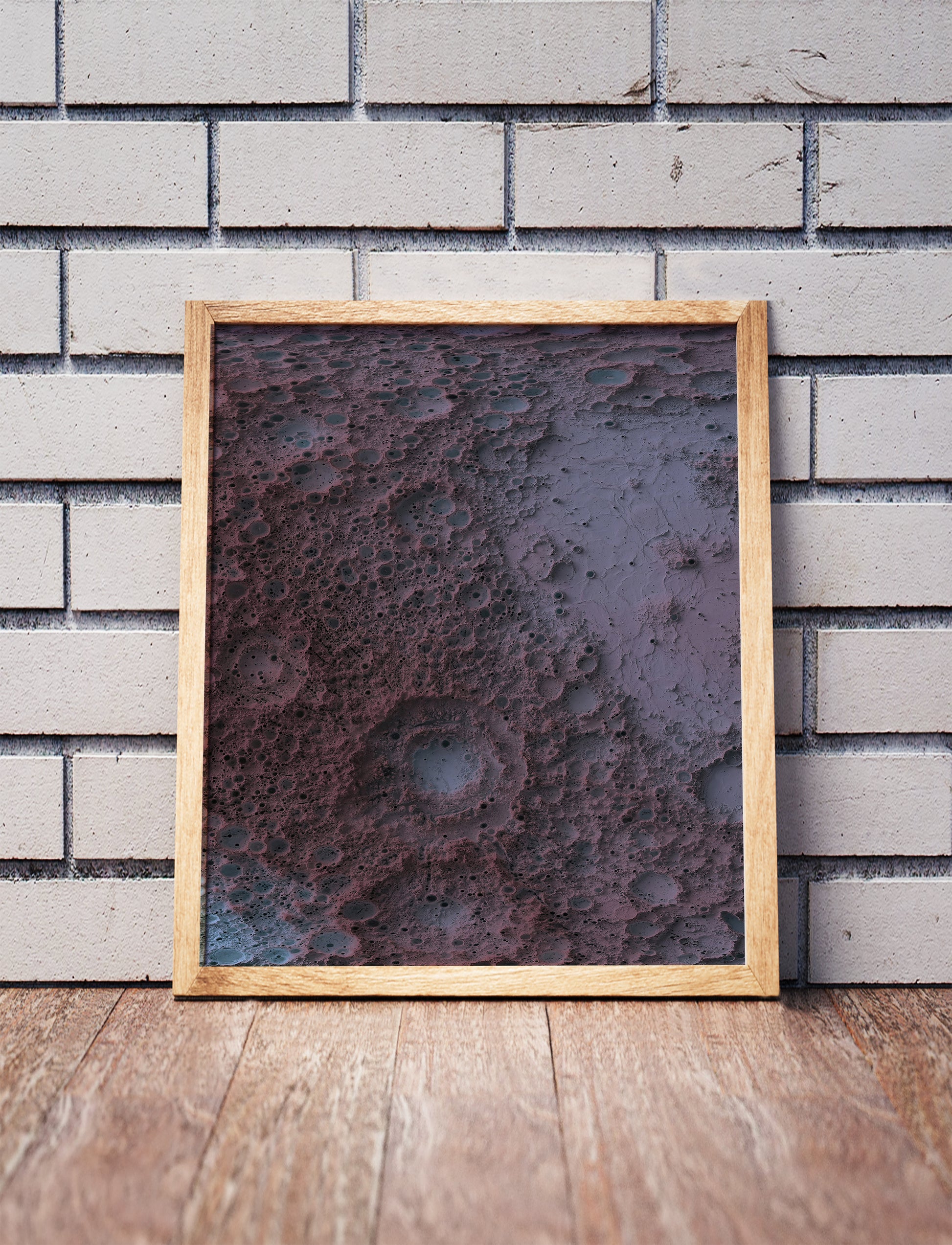 Moon shaded relief map in a wooden frame. Realistic terrain art print for home decor, displayed against a brick wall