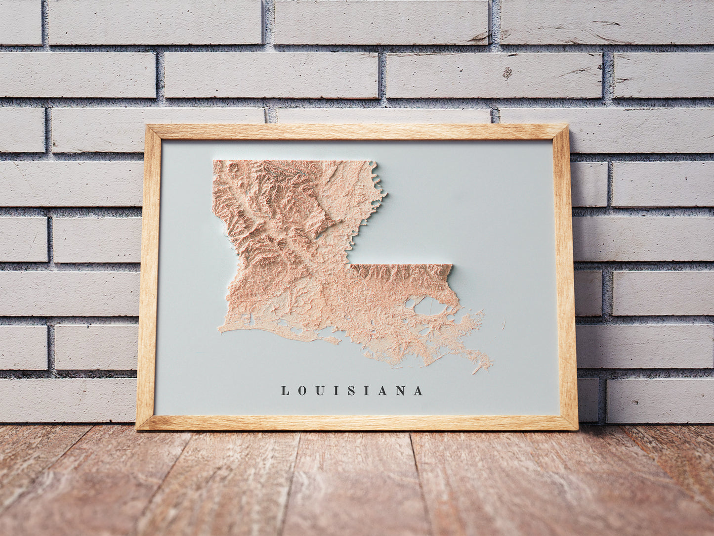 Louisiana shaded relief map in a wooden frame. Realistic terrain art print for home decor, displayed against a brick wall