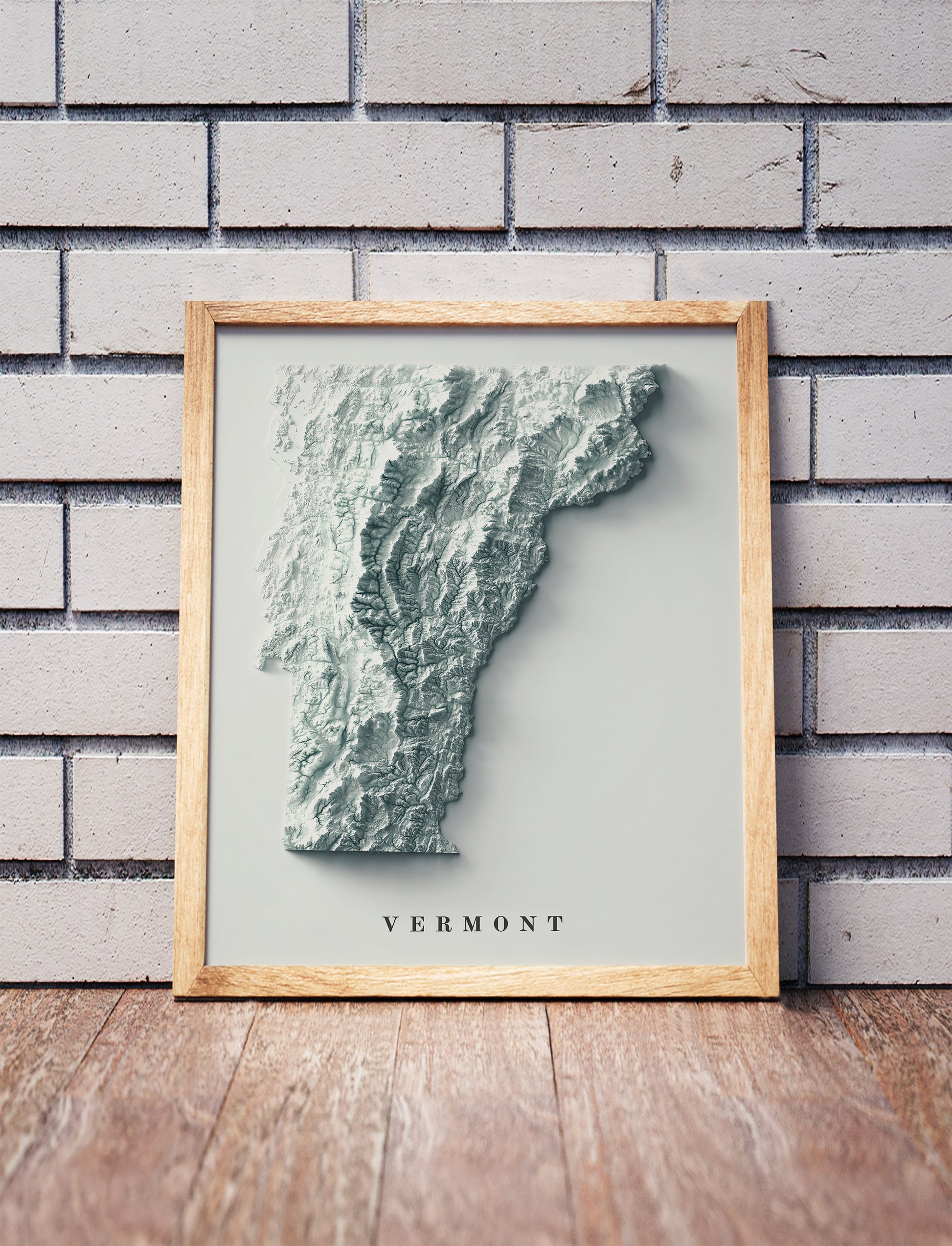 Vermont shaded relief map in a wooden frame. Realistic terrain art print for home decor, displayed against a brick wall